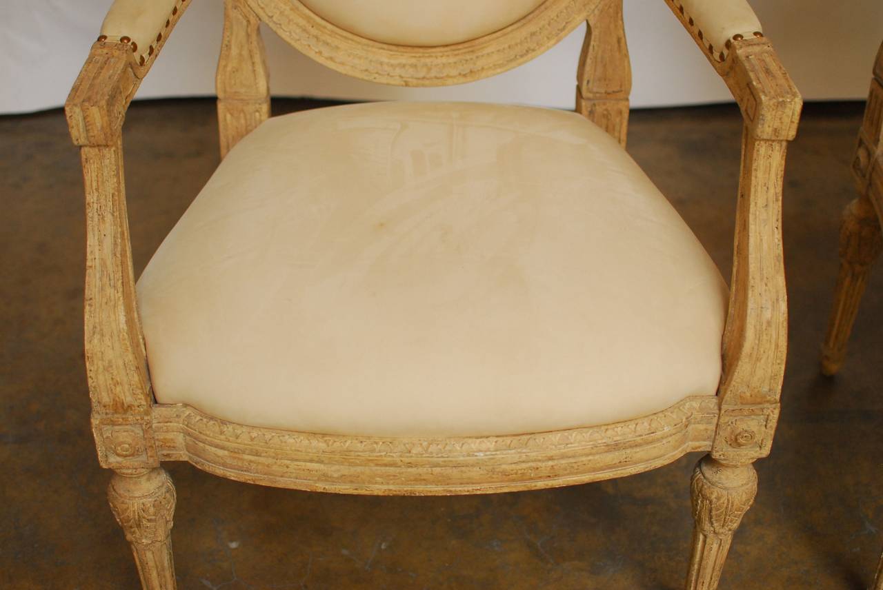 Rare pair of Moderne Fauteuils made in the Gustavian taste by Dennis and Leen of Los Angeles, California. Hand carved frame with a balloon back shape finished in a natural vintage patina finish. Upholstered in a chic bone color suede leather that is