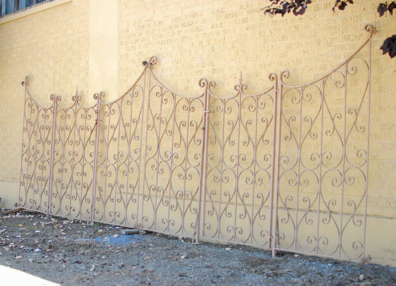 A 1920s French style antique wrought iron 6 panel garden gate fence with two swinging doors and four stationary panels. Ornate heart shaped design with fleur de lys finials and tall arch crests with scroll top details. Panels can be installed in