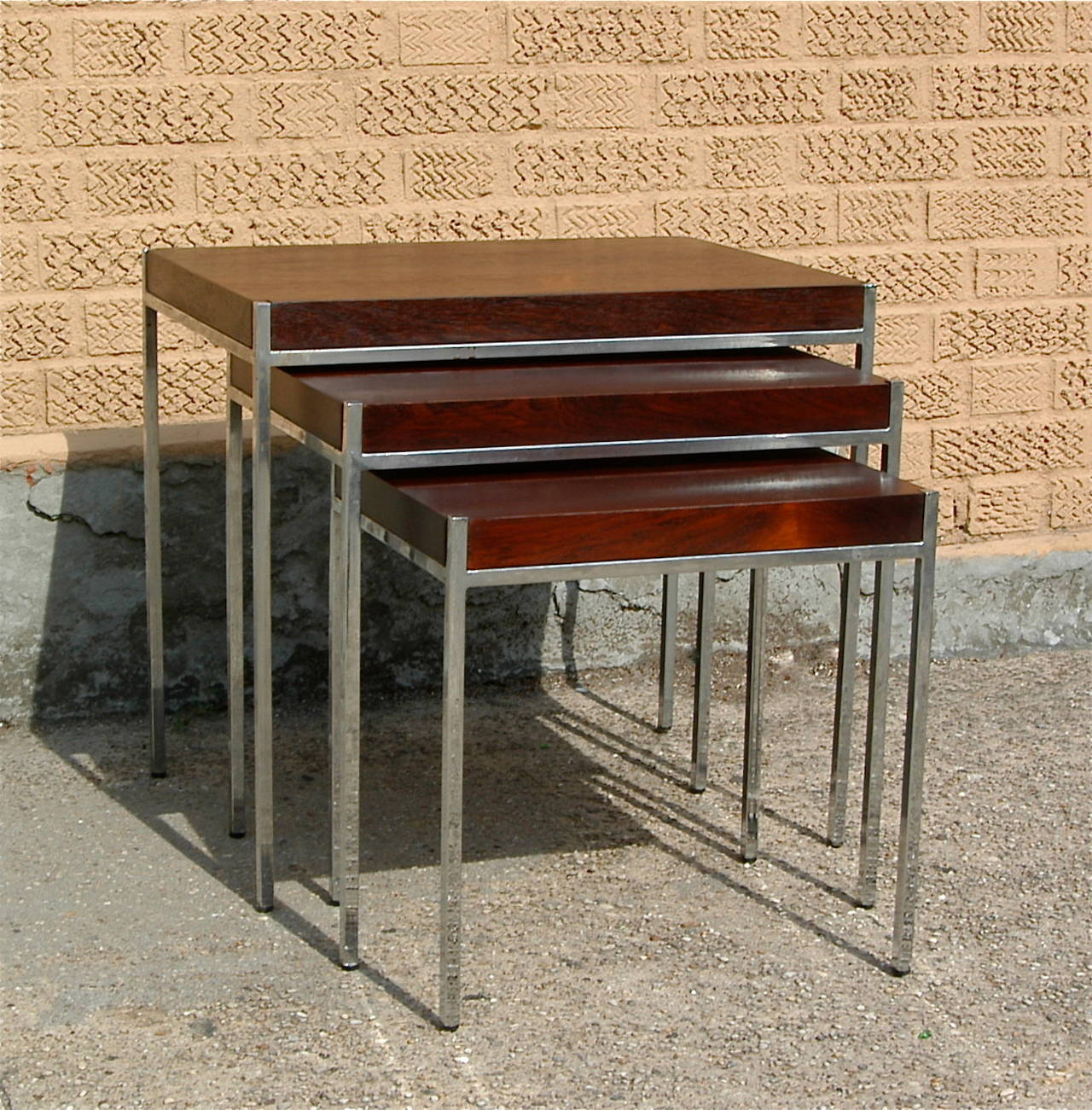 Set of three, Mid-Century Modern, nesting tables have chrome bases with inserted rosewood veneer tops in the manner of Milo Baughman.

Largest table is 21.75