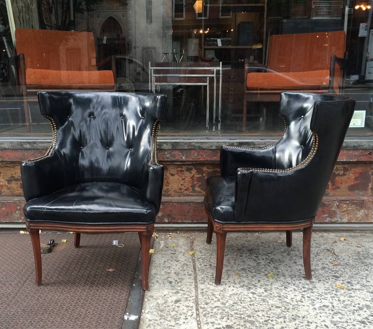 Pair of stately, black leather, high wingback, mahogany armchairs with buttoned backs and nailhead detail on the arms. There is some delicate carving on the legs. Overall patina on the chairs is fantastic.
