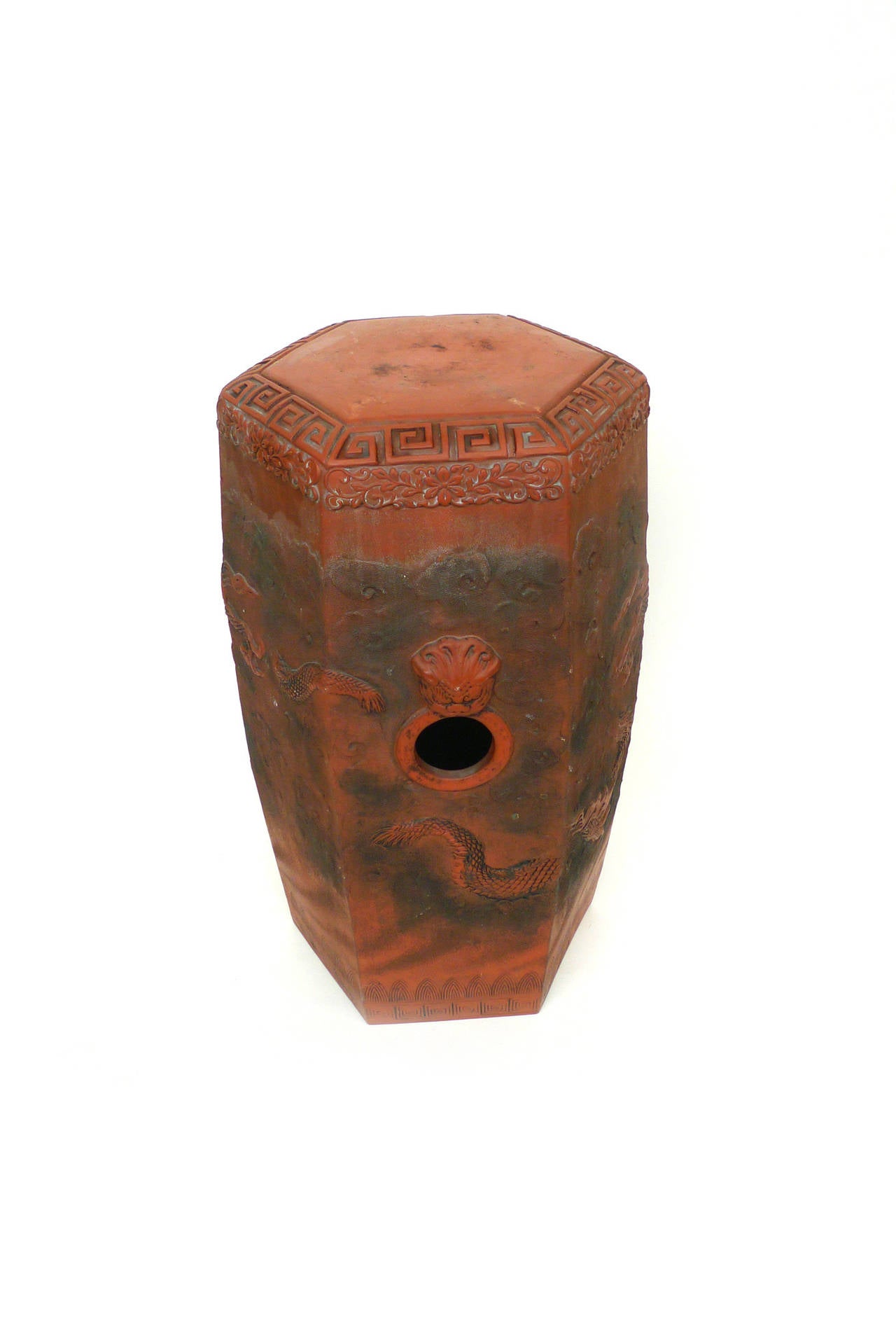 This Chinese garden seat is a beautiful red terracotta. It has a hexagonal, cylindrical shape and elaborate, richly textured designs, which include a dragon encircling the circumference, and Meander and other linear patterns.