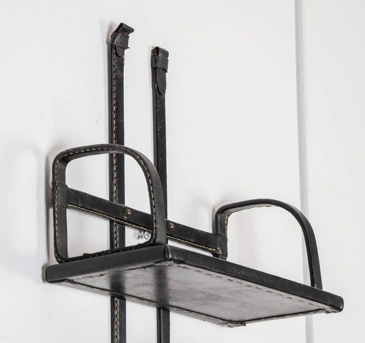 1950 wall book rack in black stitched leather by Jacques Adnet.