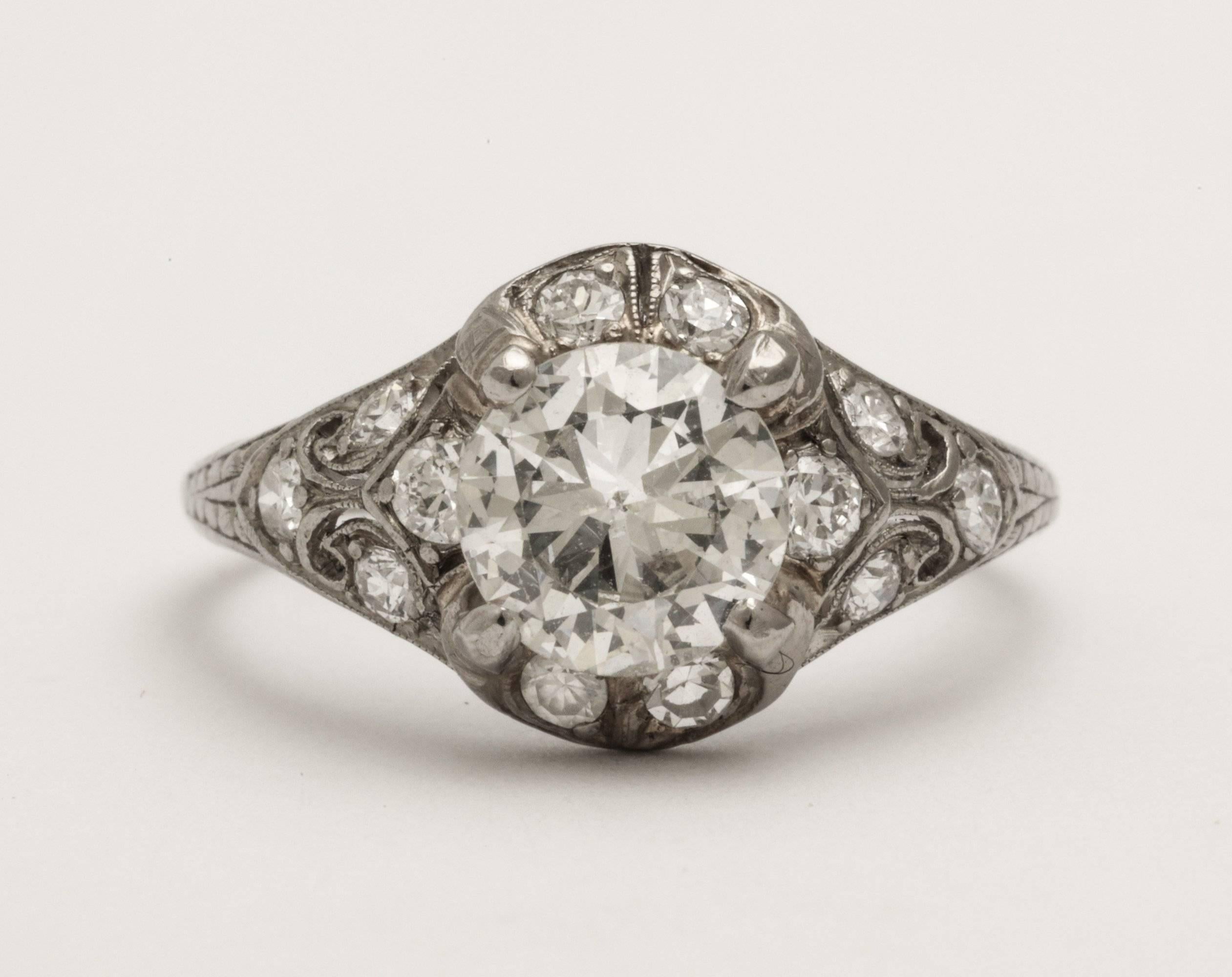 A Classic antique platinum engagement ring with a wonderful centre diamond (1.10 cts) surrounded by smaller diamonds on an elaborately decorated and pierced mount.