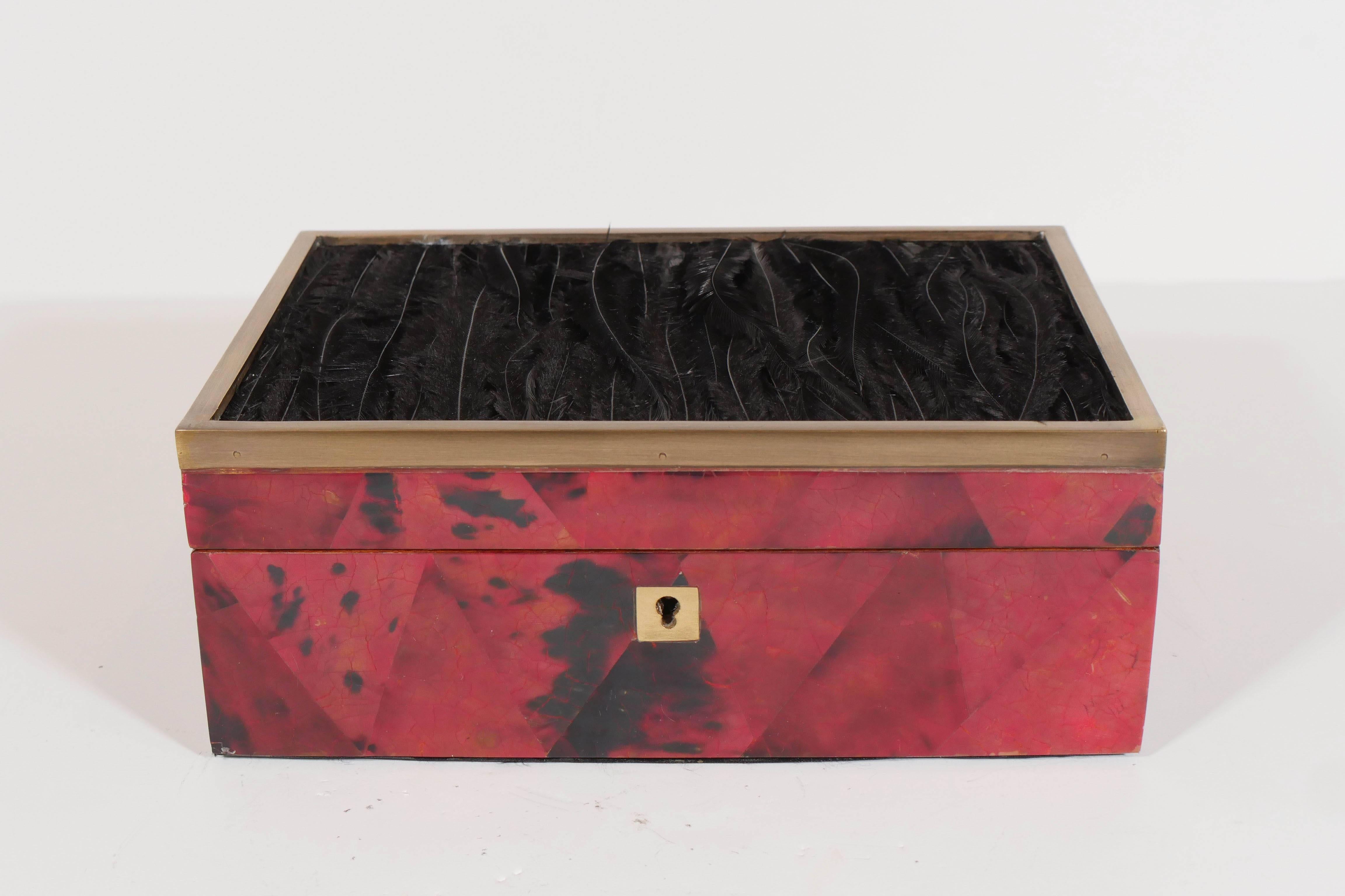 Exquisitely handcrafted jewelry box. Comprised of hand dyed and lacquered pen shell with geometric patterns in hues of ruby and black. The box has an elegant bronze hand-forged trim, and features exotic black bird feathers along the top. Fitted with