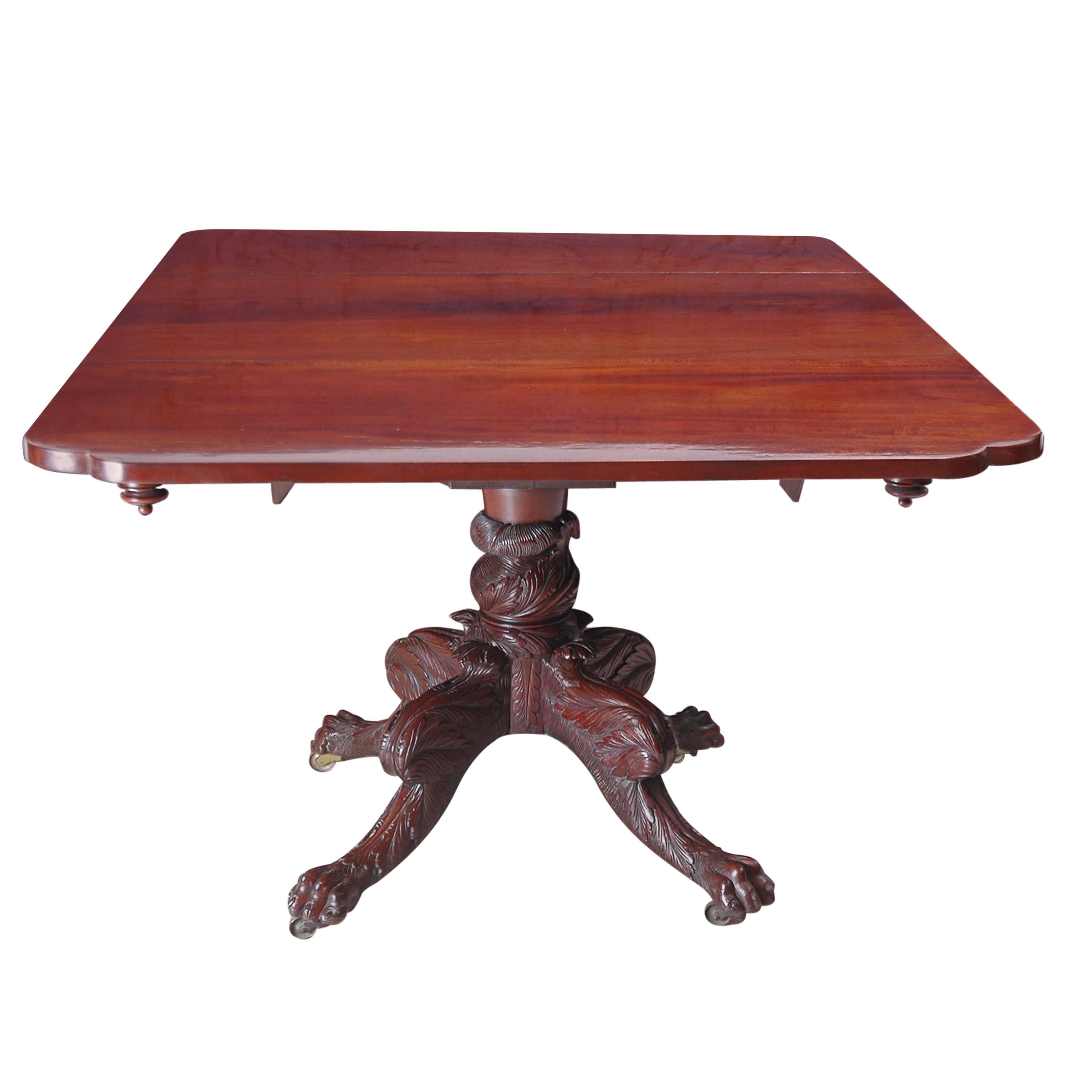 A Federal breakfast table in mahogany with a rectangular top and drop-leaves whose corners end in cyma curves, with inverted turned wooden finials. The rectangular top rests on a beautifully carved pedestal base consisting of a foliate-carved