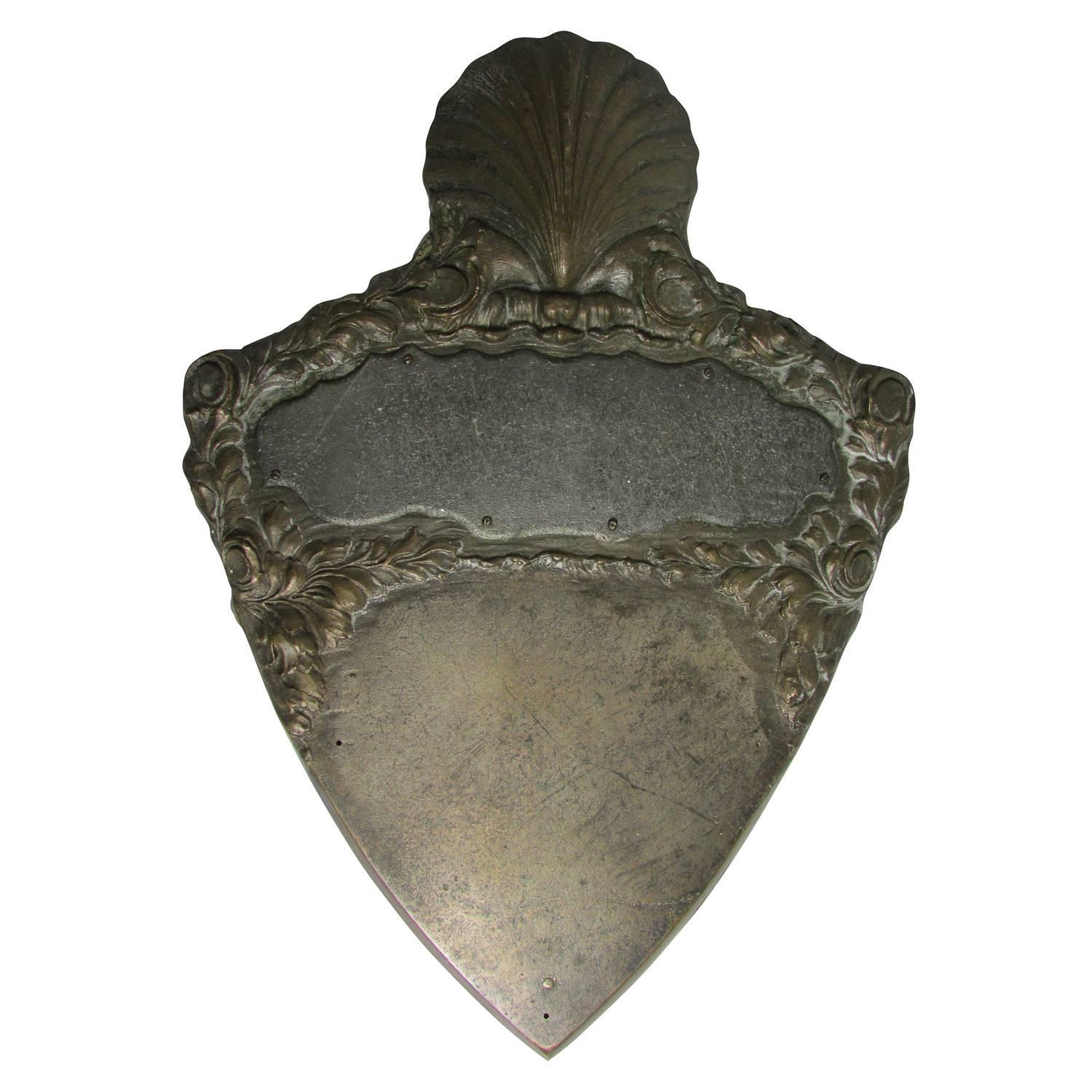 This is a lovely Victorian era shield shaped plaque that was never engraved. At the very top of the plaque is a seashell, beneath that are two blank slates for engraving.