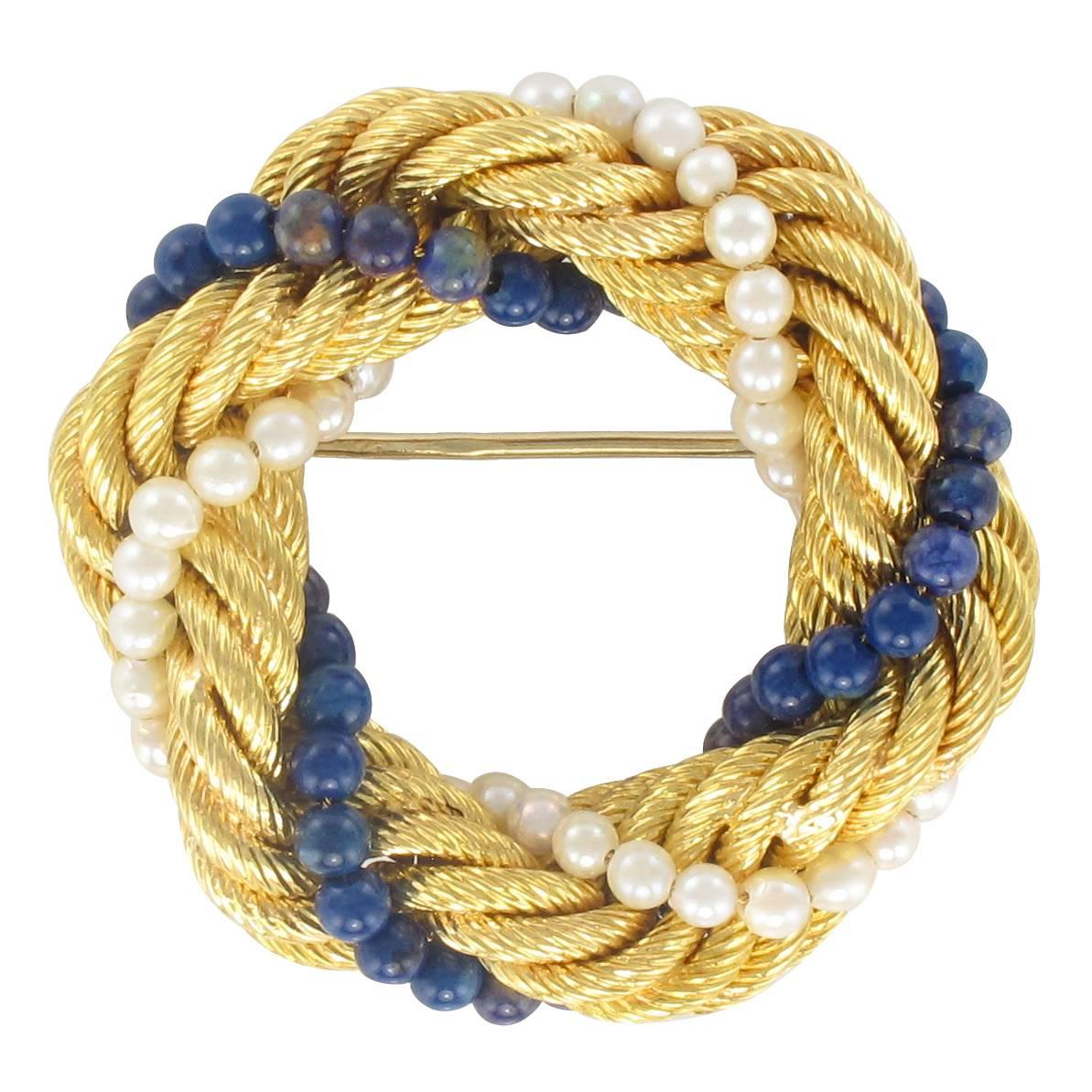Brooch in 18 carat yellow gold. 
This splendid round antique brooch is composed of a golden twisted rope entwined with a strand of small white cultured pearls and a strand of small lapis lazuli beads. The clasp is a pin. 
Diameter of pearls: 3