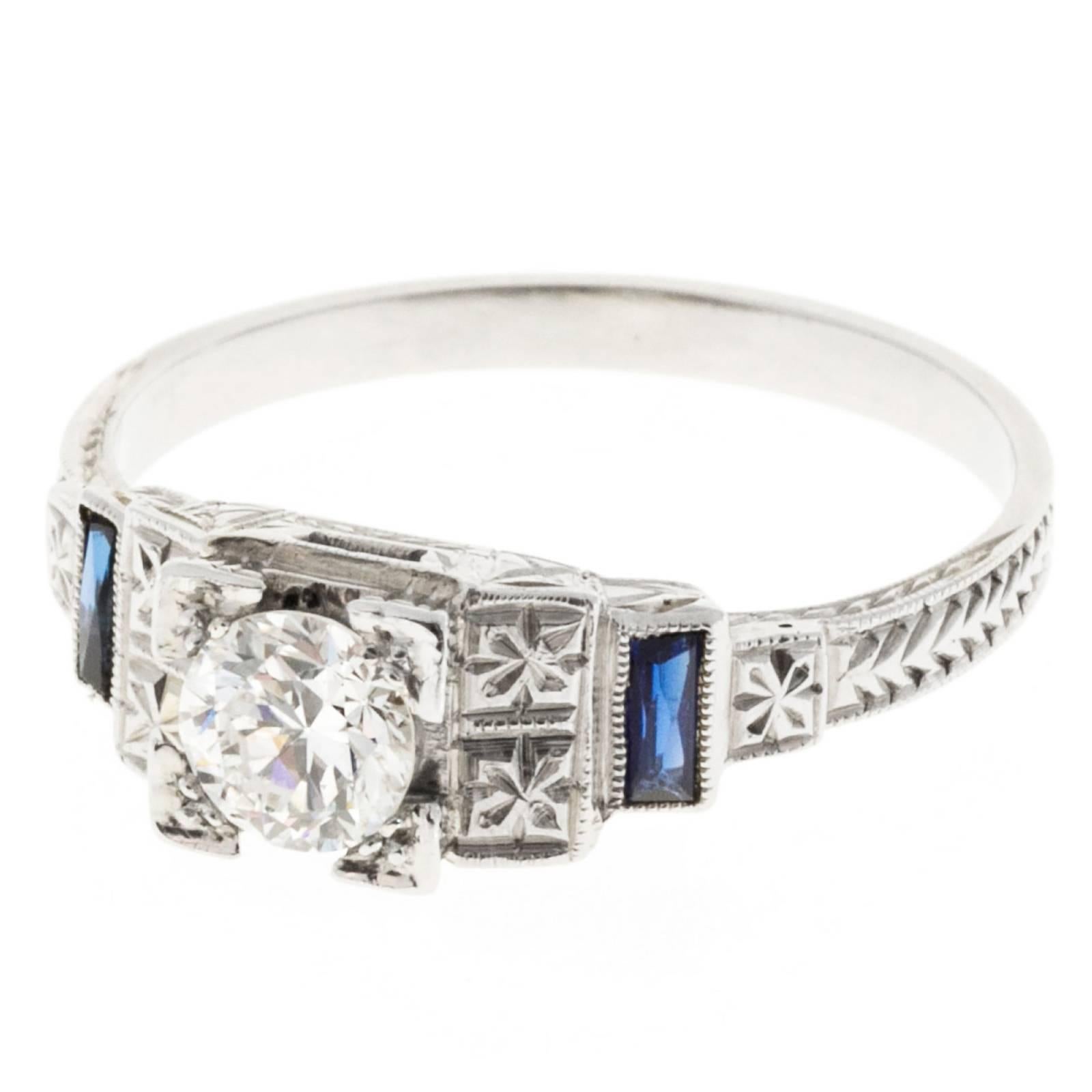 1940's 18k white gold Art Deco engraved ring with a center diamond and two side baguette sapphires. 

One  .45ct, E to F color and VS1 clarity, Ideal cut. Depth: 61.9% Table 58%
2 Calibre Swiss cut baguette Sapphires .12ct total.  4.2mm
Size 7 1/2