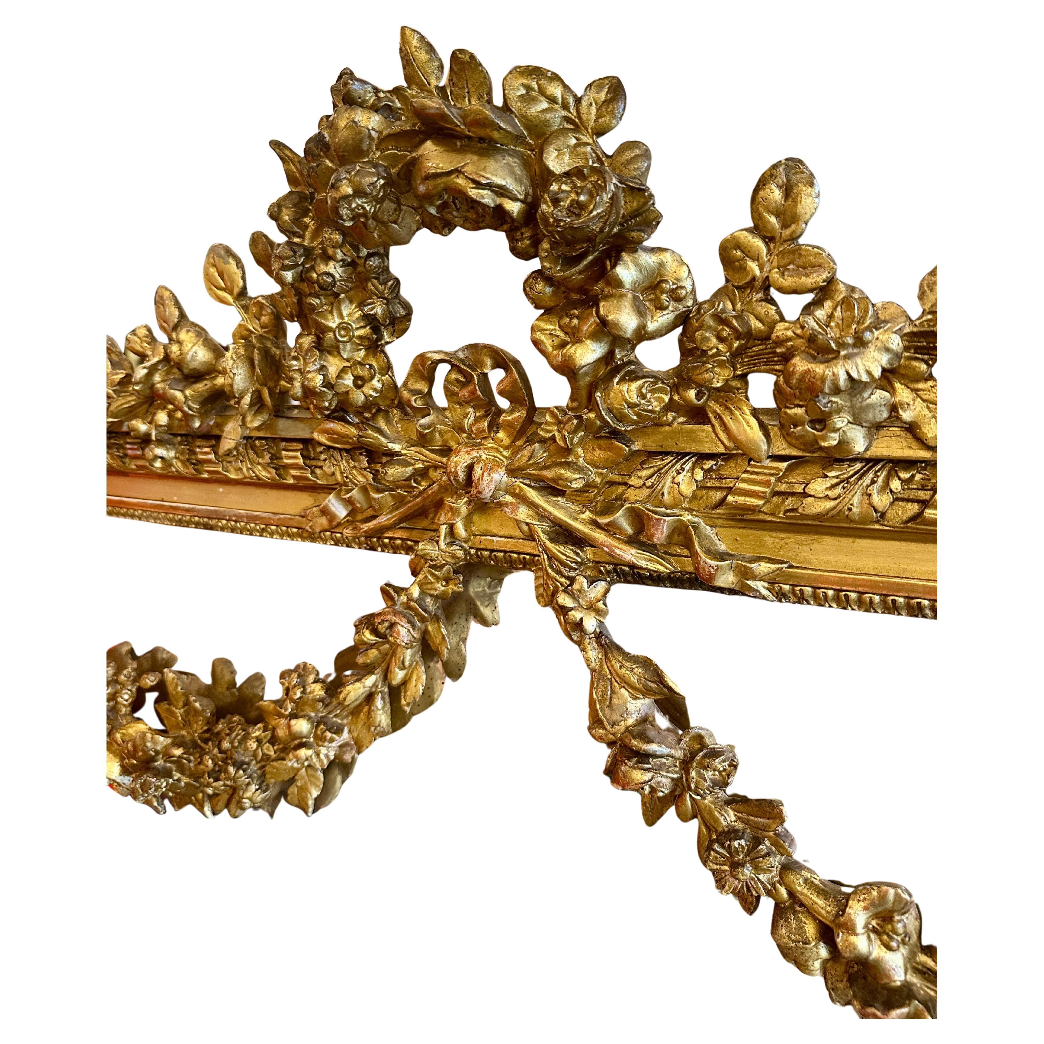 Un grande specchio ornato francese in stile Luigi XVI. La parte superiore è crestata da un grande arco floreale foliato che sovrasta un fiocco legato con un nastro e una faretra con festoni floreali sulle spalle sostenuti da rosette. La cornice è