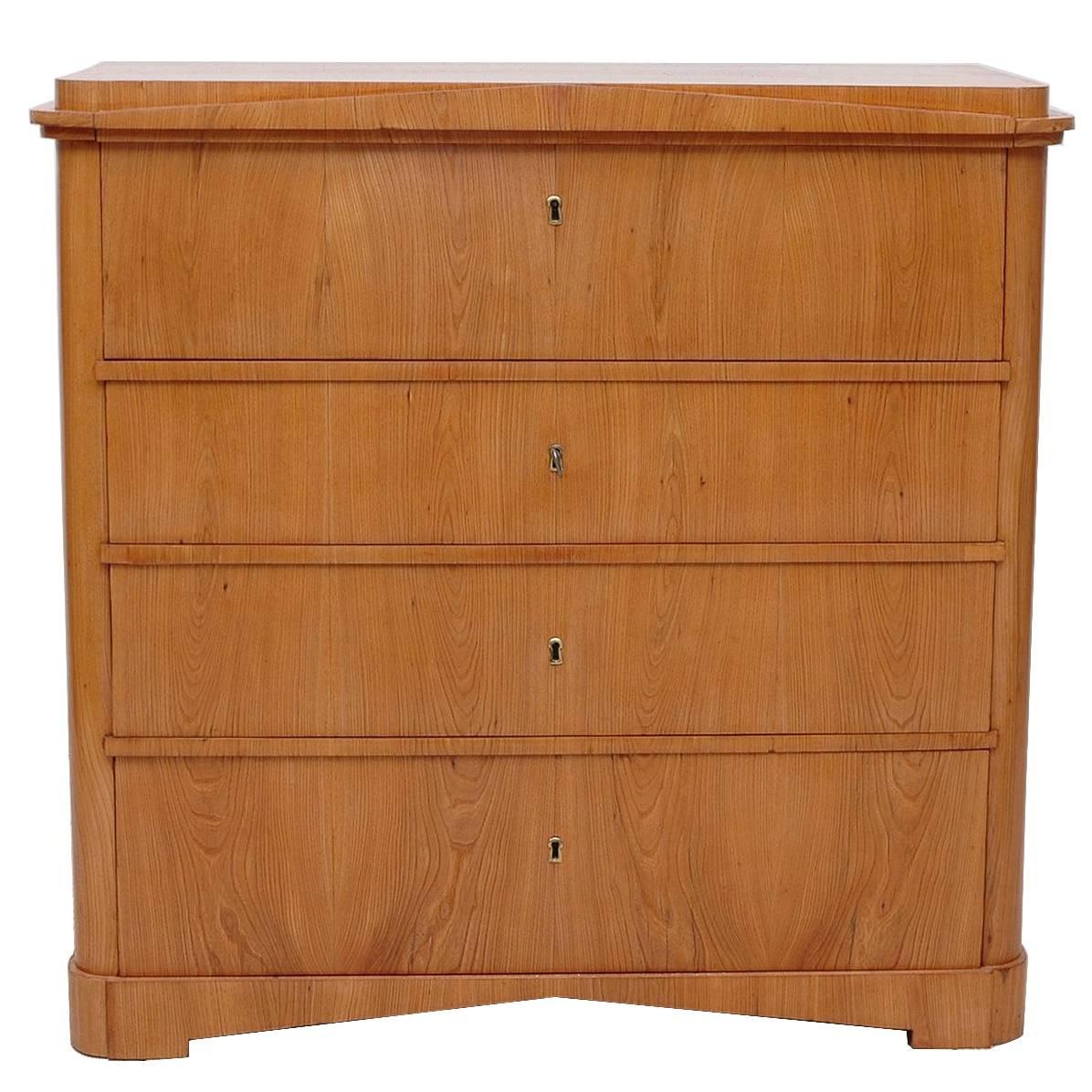 A handsome small North German Biedermeier chest of drawers with four drawers. Top drawer folds opens to a secretary desk housing an open cubby surrounded by eight small drawers. In beautiful bookmatched ashwood with pediment top and bracket feet,