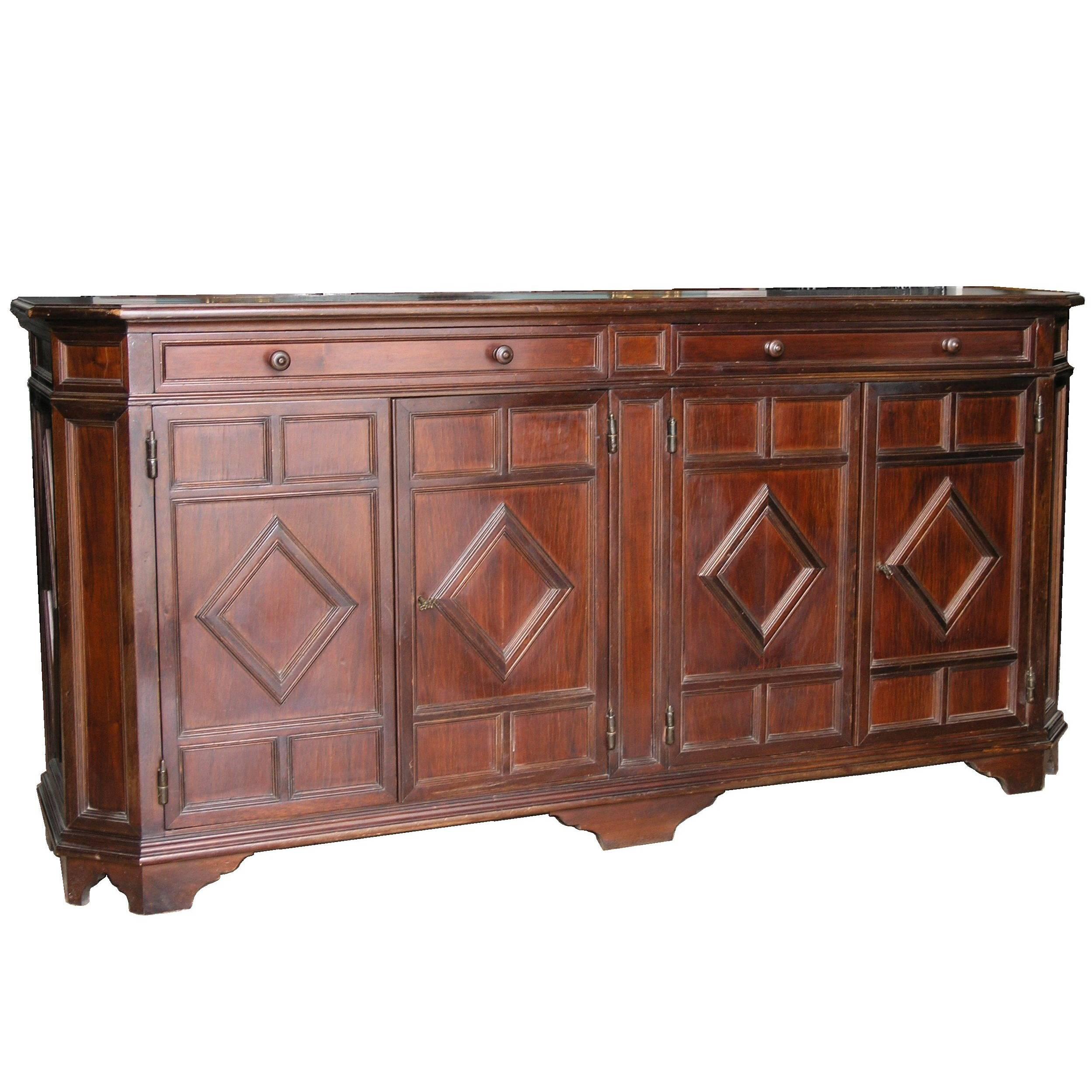 The rectangular top with canted angles and molded edge, the conforming case fitted with two long drawers above four doors carved with diamond-shaped motifs, raised on a molded base with bracket feet.