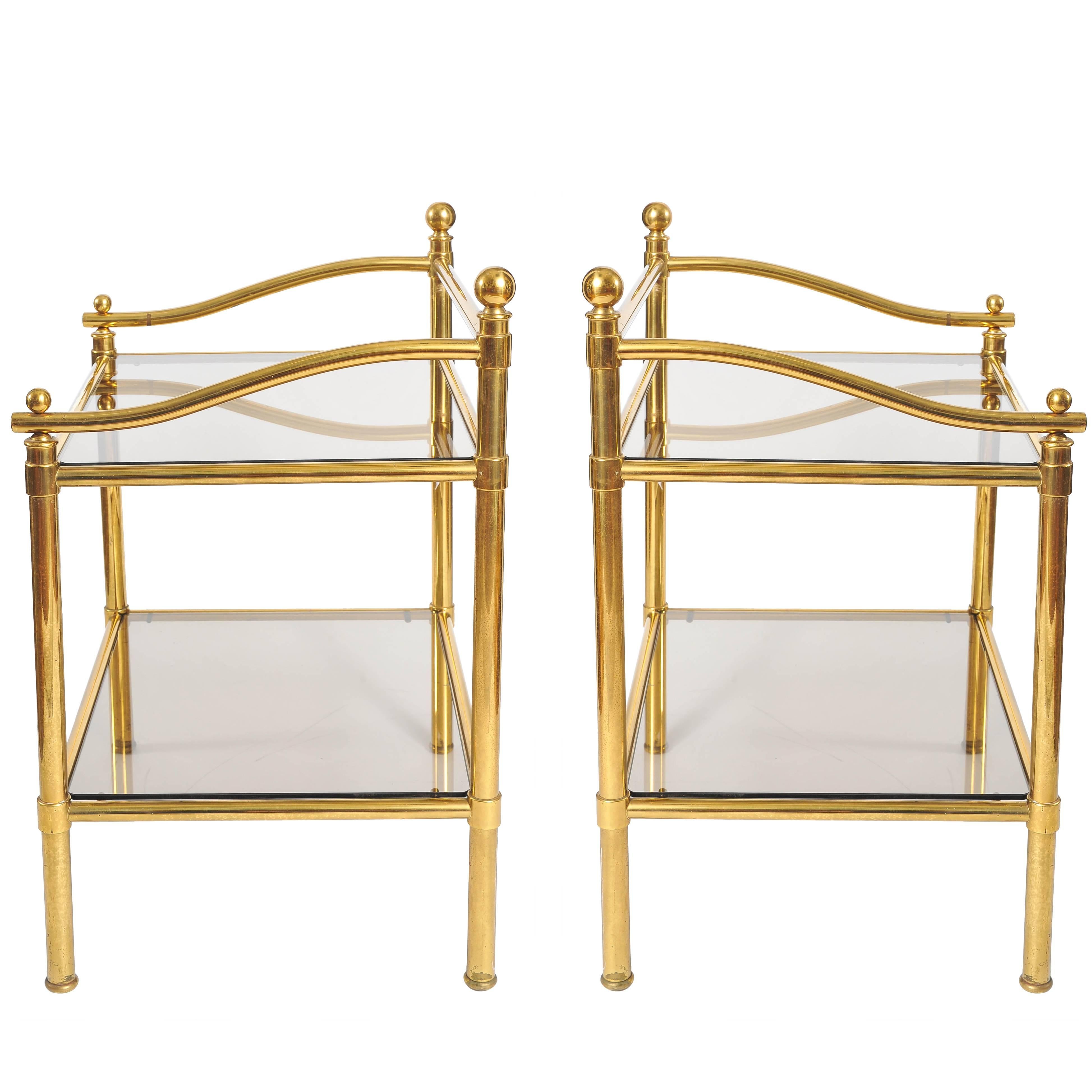 Elegant brass side tables with decorative curved sides and raised back frame, finished with brass finials. Two shelves of smokey glass.