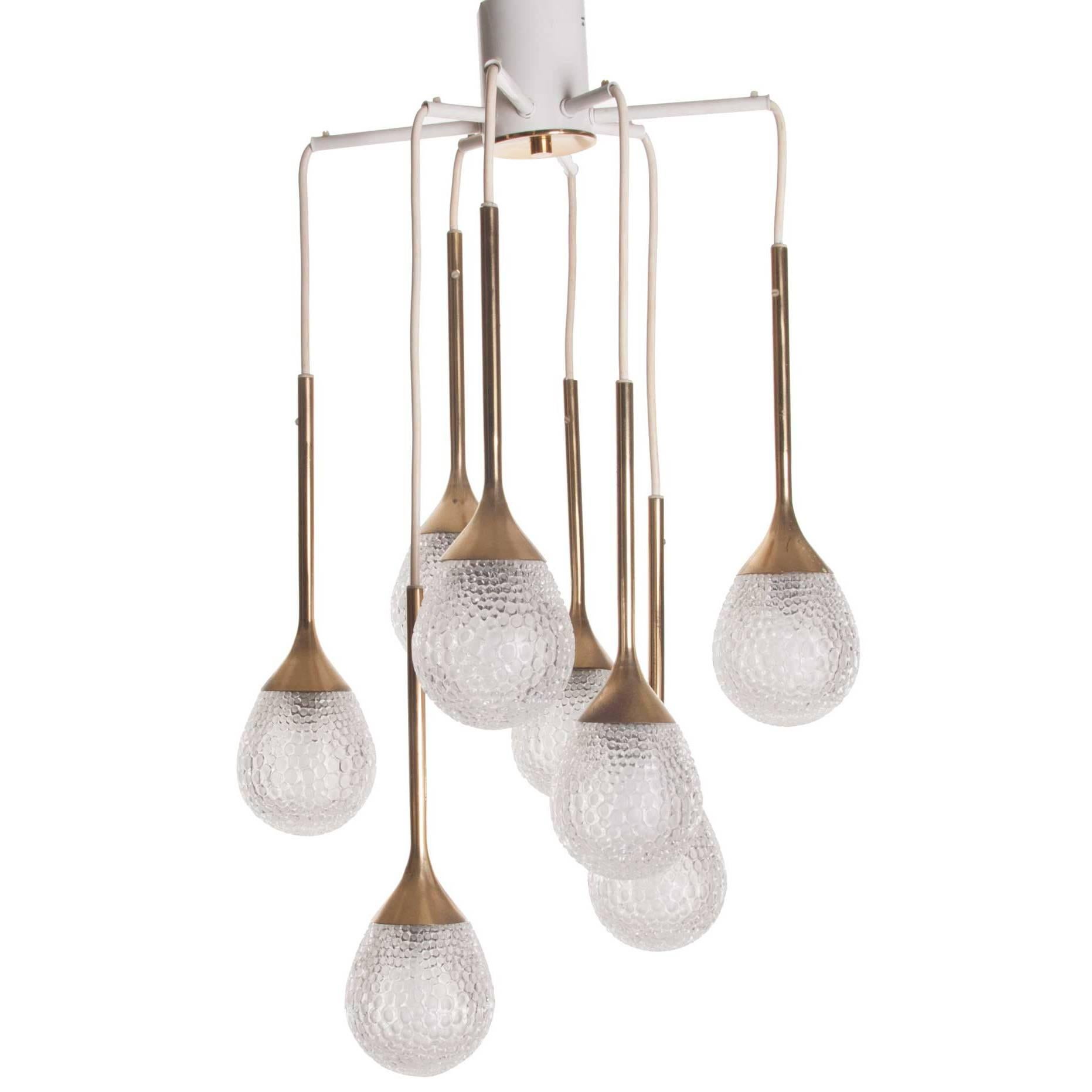 Stunning chandelier consists of eight lights and arms with beautiful pressed glass drops. The combination of the brass stem, glass drops and random length of the stem makes it an eye-catcher!