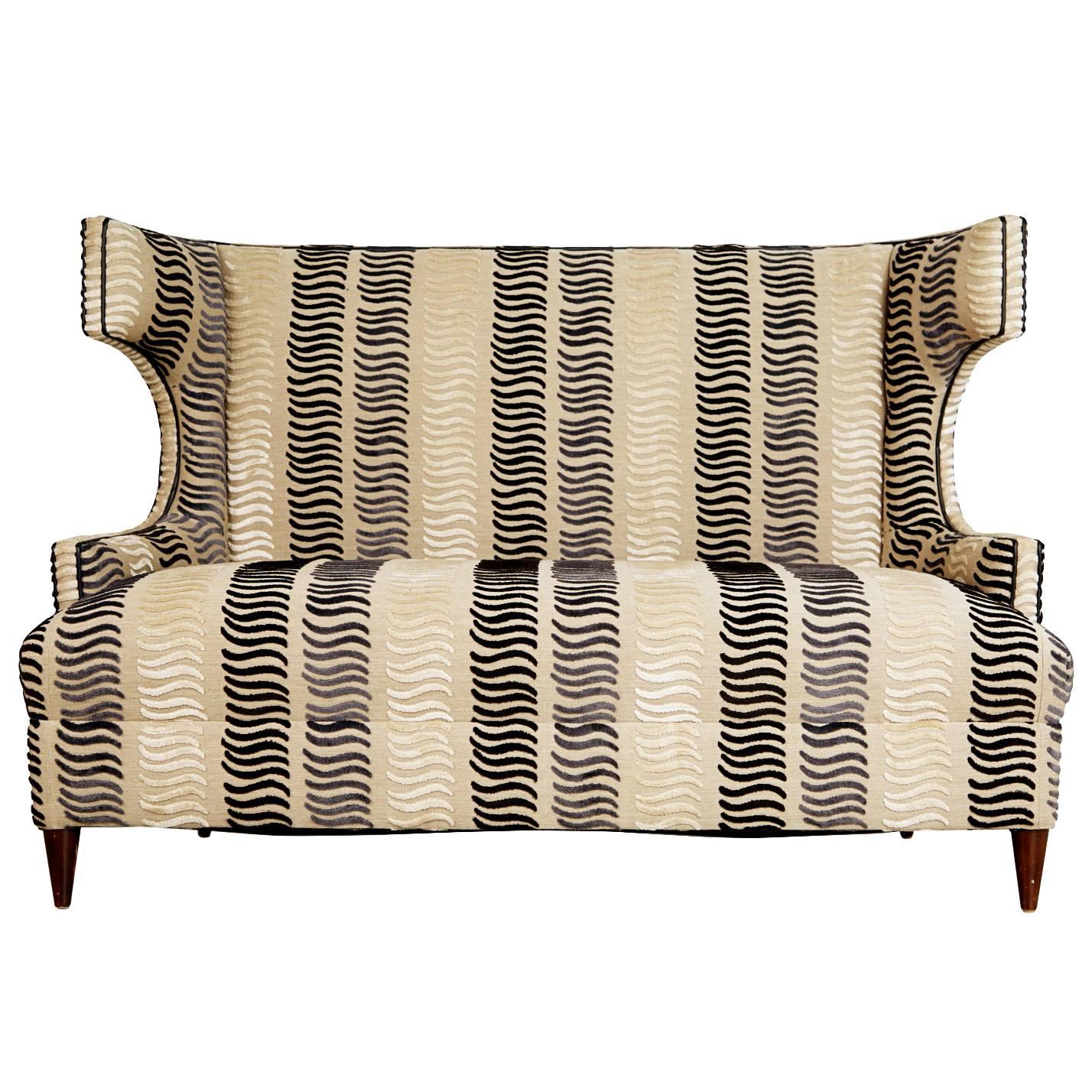 Sculptural wingback loveseat that will surely grab the attention of your guests. Recently upholstered in a high end fabric featuring lineal layers of cut velvet forming alternating stripe Formations in shades of ivory, soft mauve with gray