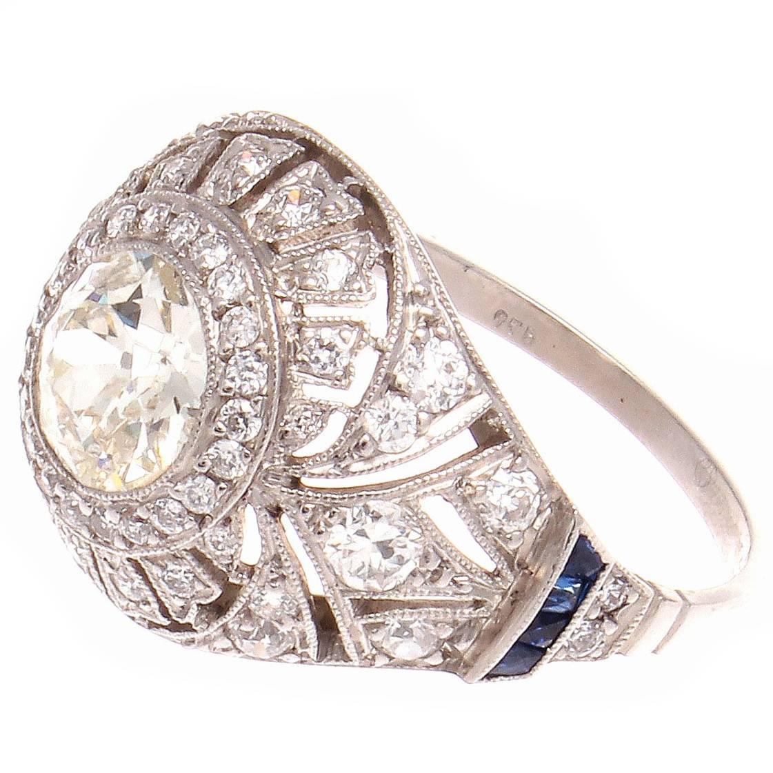 The allure of the Art Deco time period has inspired the creation of this intricately designed dome ring. Featuring a charming  1.13 carat old European cut diamond that is surrounded by strategically  placed matching diamonds and vibrant blue