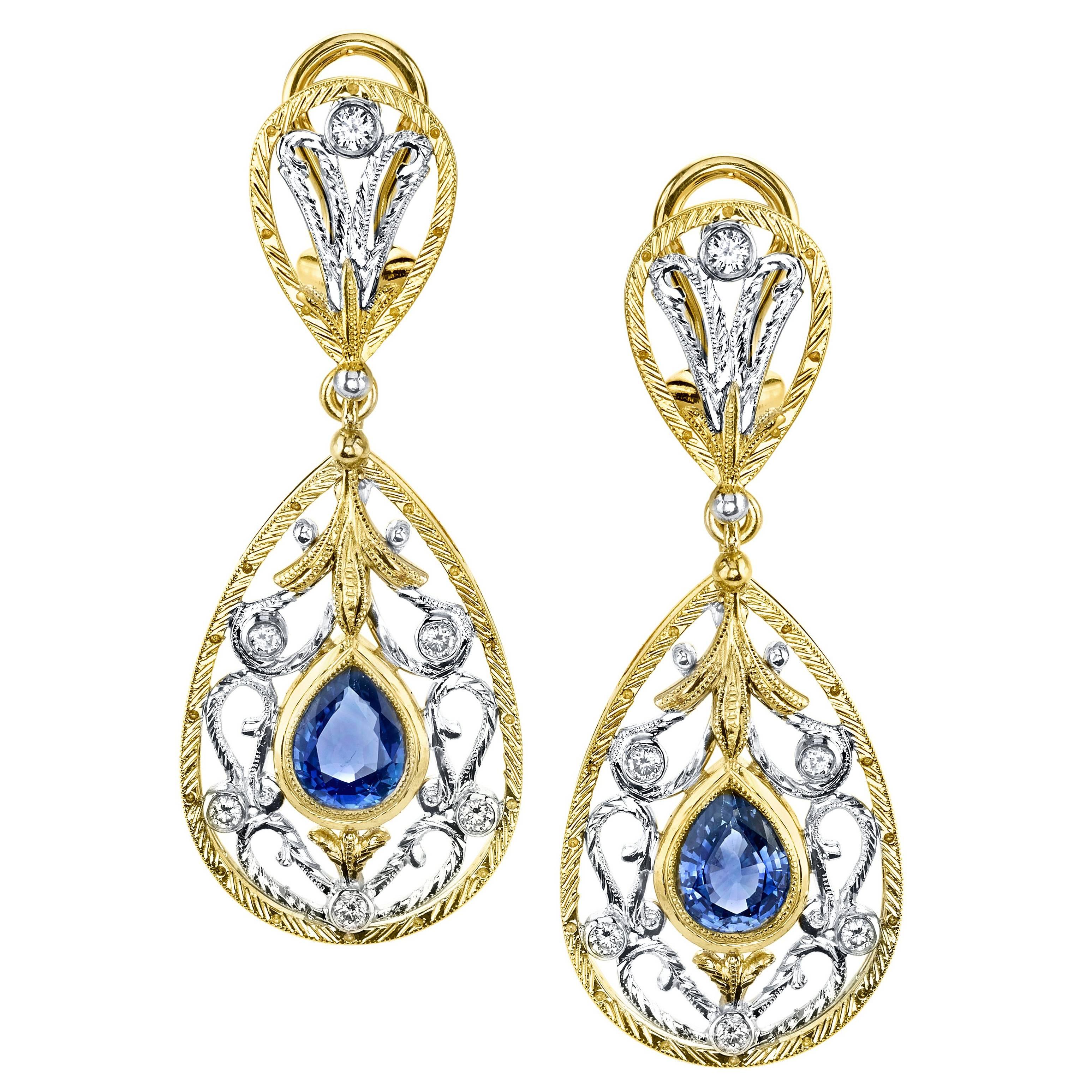 These intricately designed and handcrafted dangle earrings feature beautifully matched pear shaped royal blue sapphires set with sparkling diamonds in a stunning and elaborate design! The sapphires are bezel set in 18k yellow gold, framed with