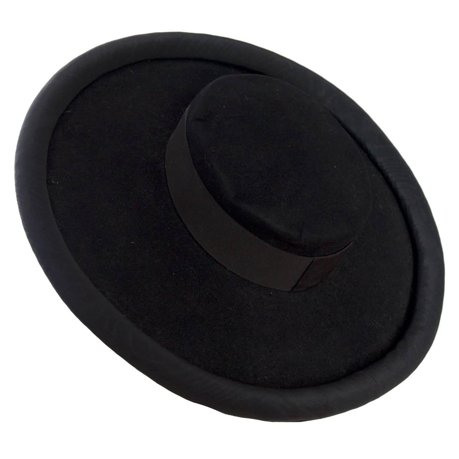 A 1980s black Yves Saint Laurent - Rive Gauche wide brimmed felt hat with a wide grosgrain bands and a round pipe style trim around the brim. A thin matching black ribbon can be tied around the chin. 

Model: A517
The hat is a size 56 1/2