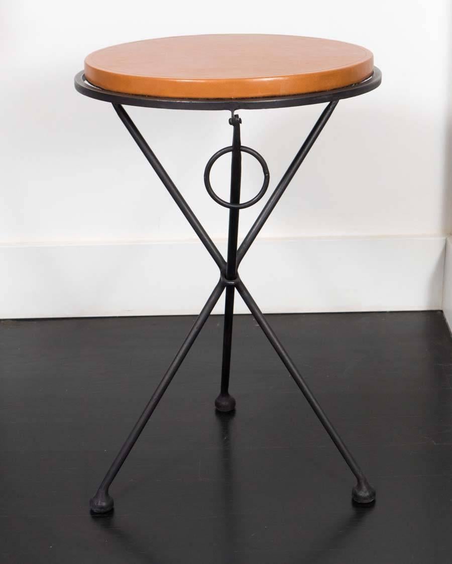Pair of occasional tables from France. Hand forged iron base with leather covered oak tops. Once lifted by the rings, these tables fold flat.