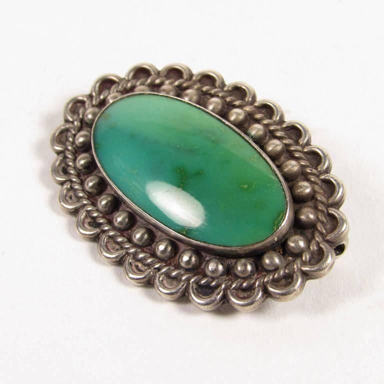 Vintage 20th century Native American Navajo sterling silver and turquoise brooch. Oval with scalloped edge and beaded silver setting containing a turquoise stone. 
Measures: Length 1 3/8 inches, width 1 inch.
