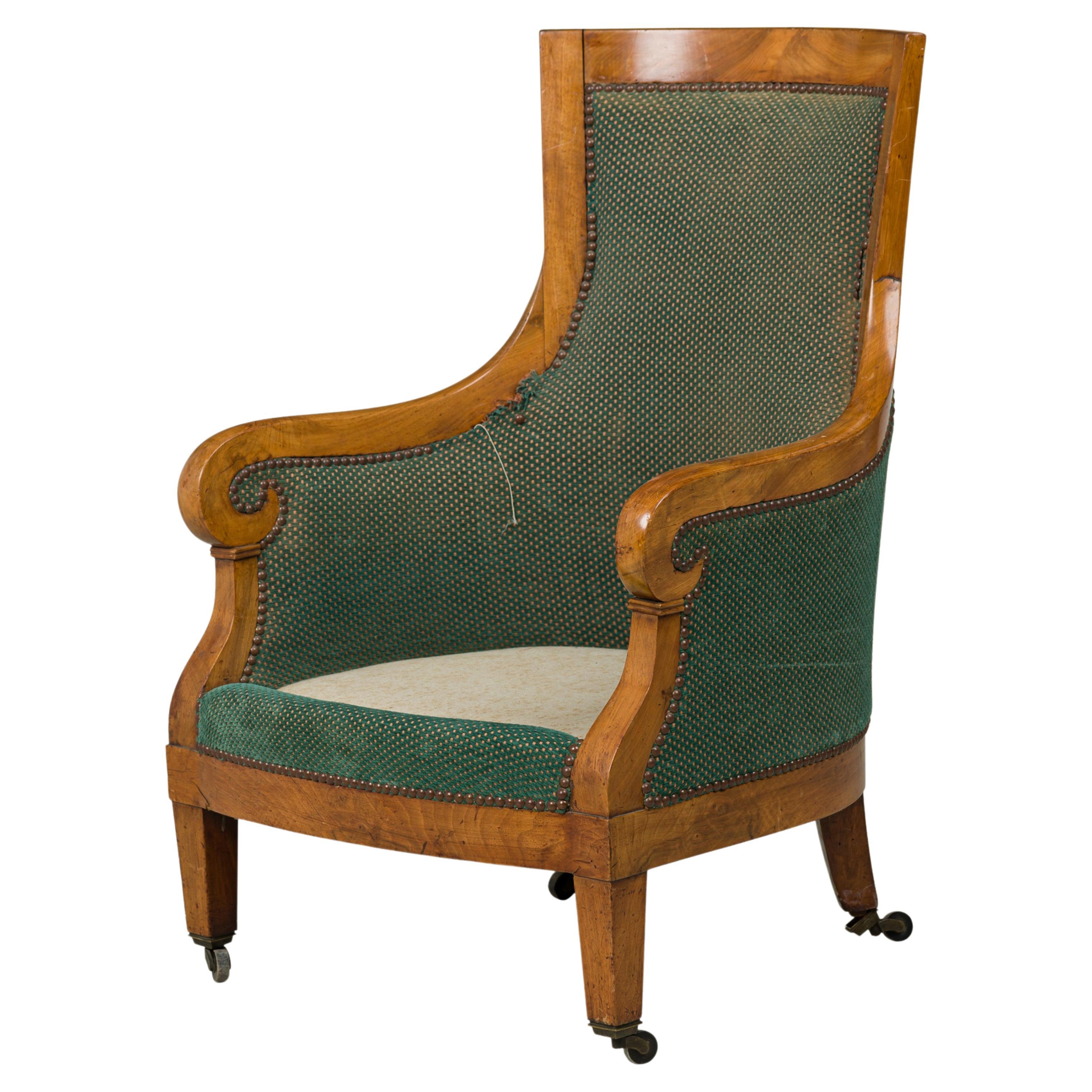 Austrian Biedermeier birch veneer bergere armchair with a slightly flared back and scroll design arms, upholstered in a textured green and beige fabric with bronze nailhead trim, resting on four tapered square legs ending in small metal casters.