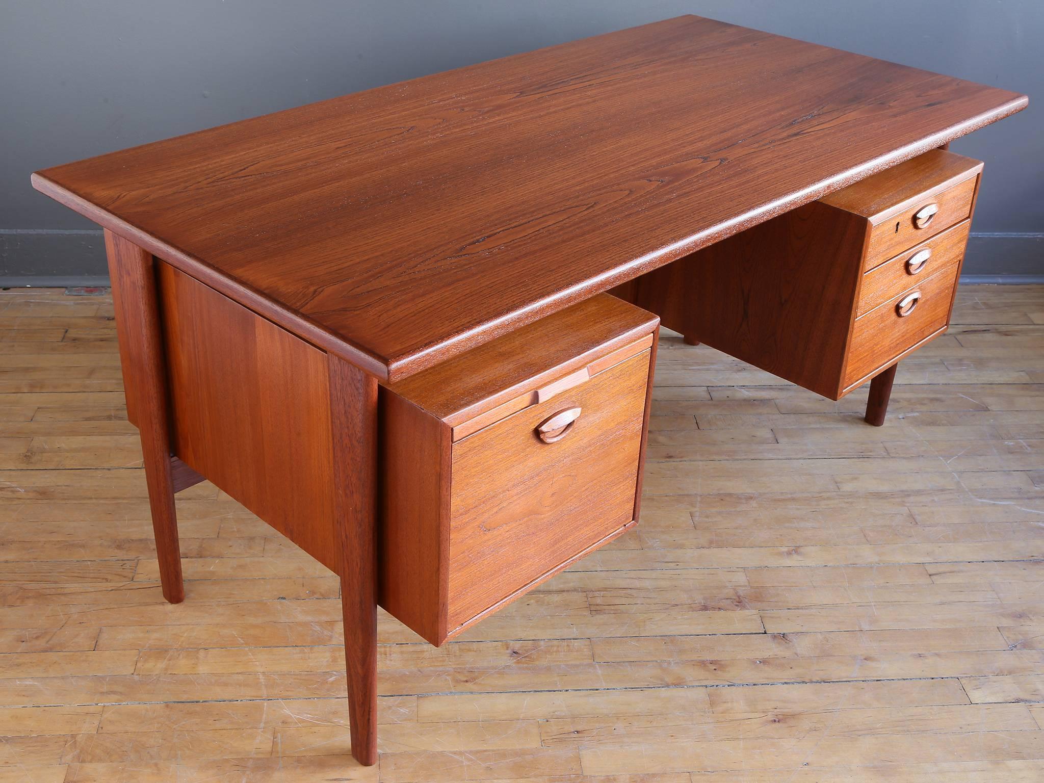 A teak executive's desk by Danish designer Kai Kristiansen, circa 1950s. Featuring a floating top supported by tapered, solid teak legs. The left side with a large file drawer and pull-out writing surface, while the right side has three graduated