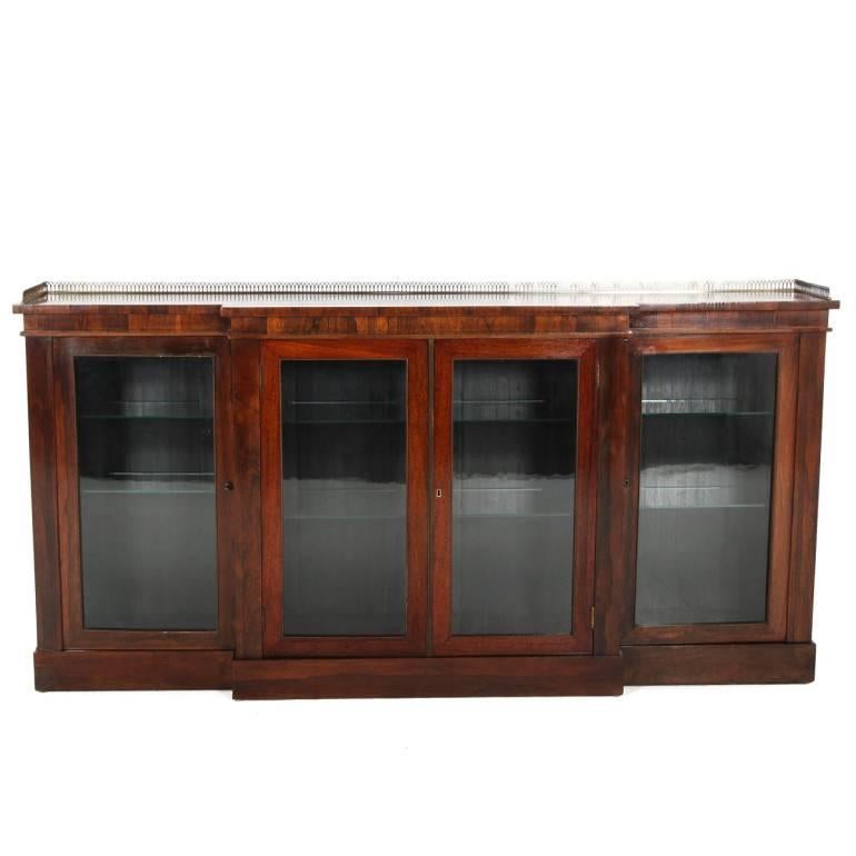 Elegant with beautiful patina, we present this early 19th century English rosewood bookcase with bronze gallery, original glass doors, with new glass shelving. This is a stunning piece in beautiful condition.