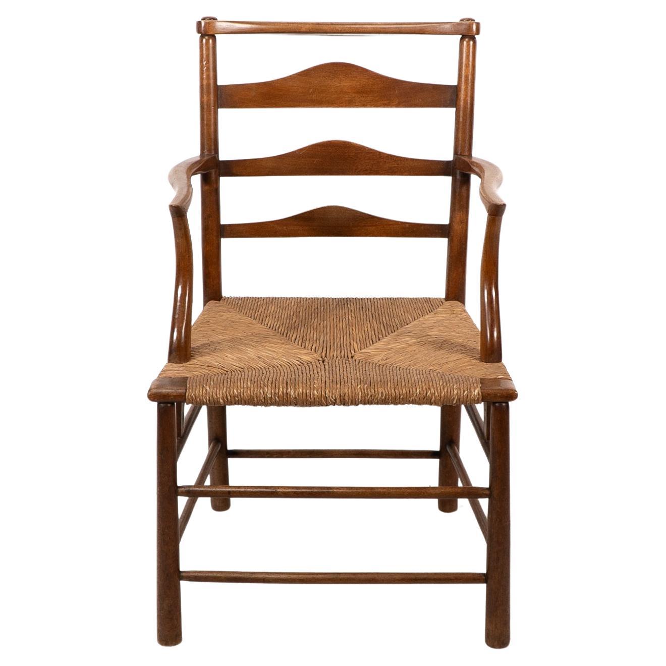 C. R. Ashbee. Sillón Arts and Crafts de asiento de junco y respaldo de escalera, con brazos que bajan hasta las camillas laterales. Ashbee utilizó esta versión de sillón para su casa familiar, oficinas y taller personal que construyó en el número 37