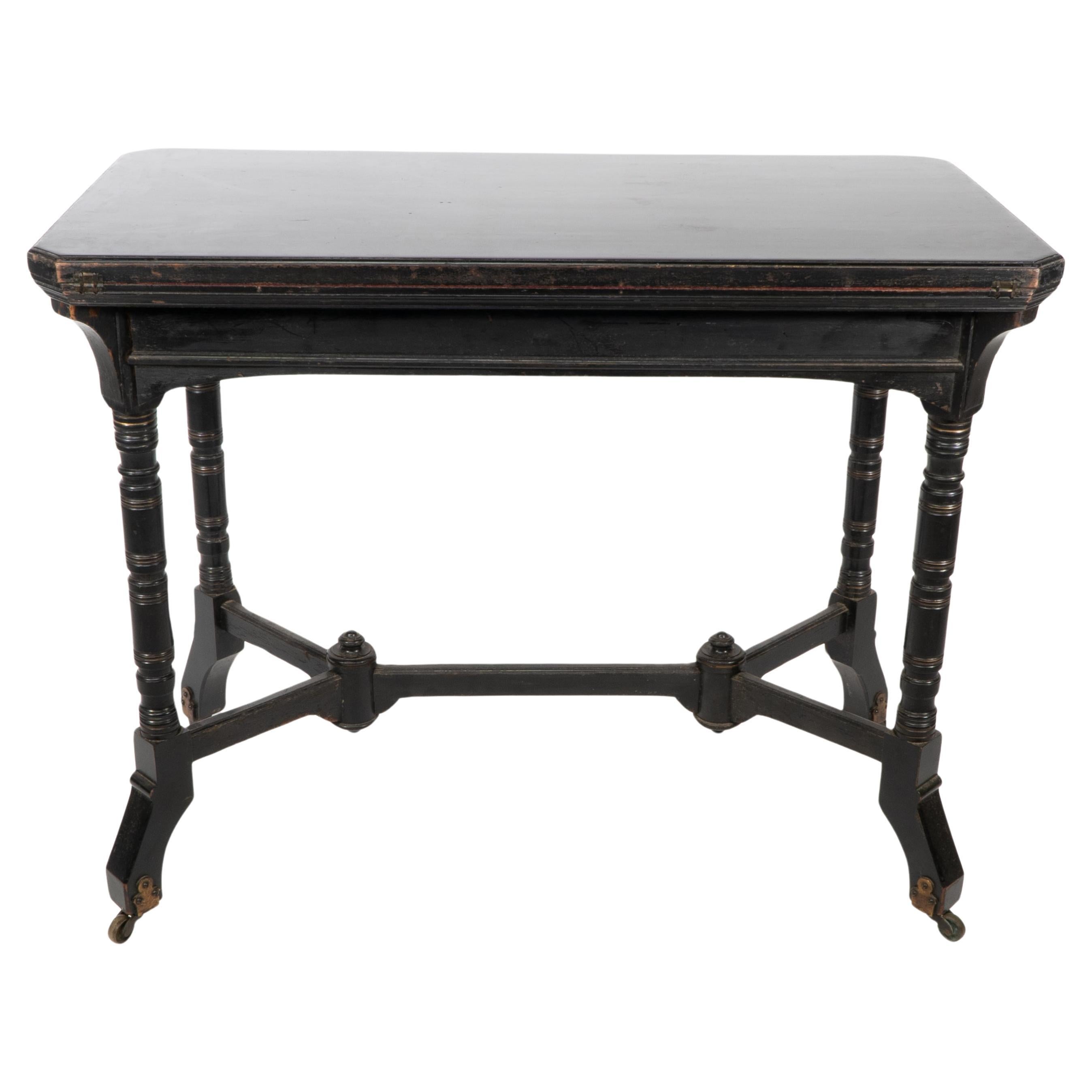 Charles Bevan, made by Marsh Jones and Cribb. An Aesthetic Movement Walnut ebonized card table with fold over top retaining the original red baize on turned legs united by a double wishbone stretcher on high decorative brass castors. Unfolded: H 72