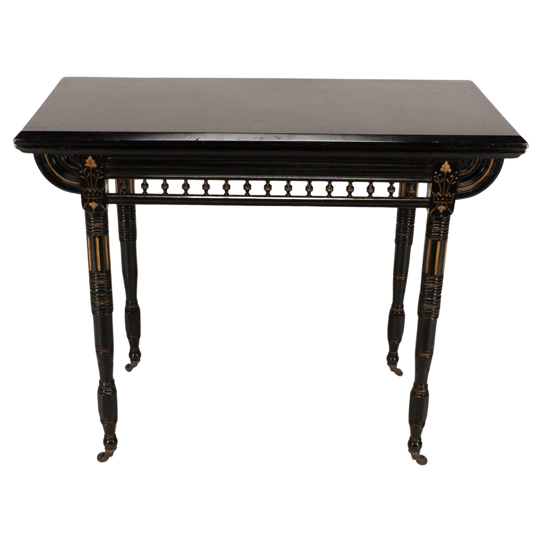 Gillows attributed. An Aesthetic Movement ebonized games and card table with deeply incised and gilded crown and floral decoration to the apron with a turned gallery below to each side. The top swivels and opens to reveal a storage area for games