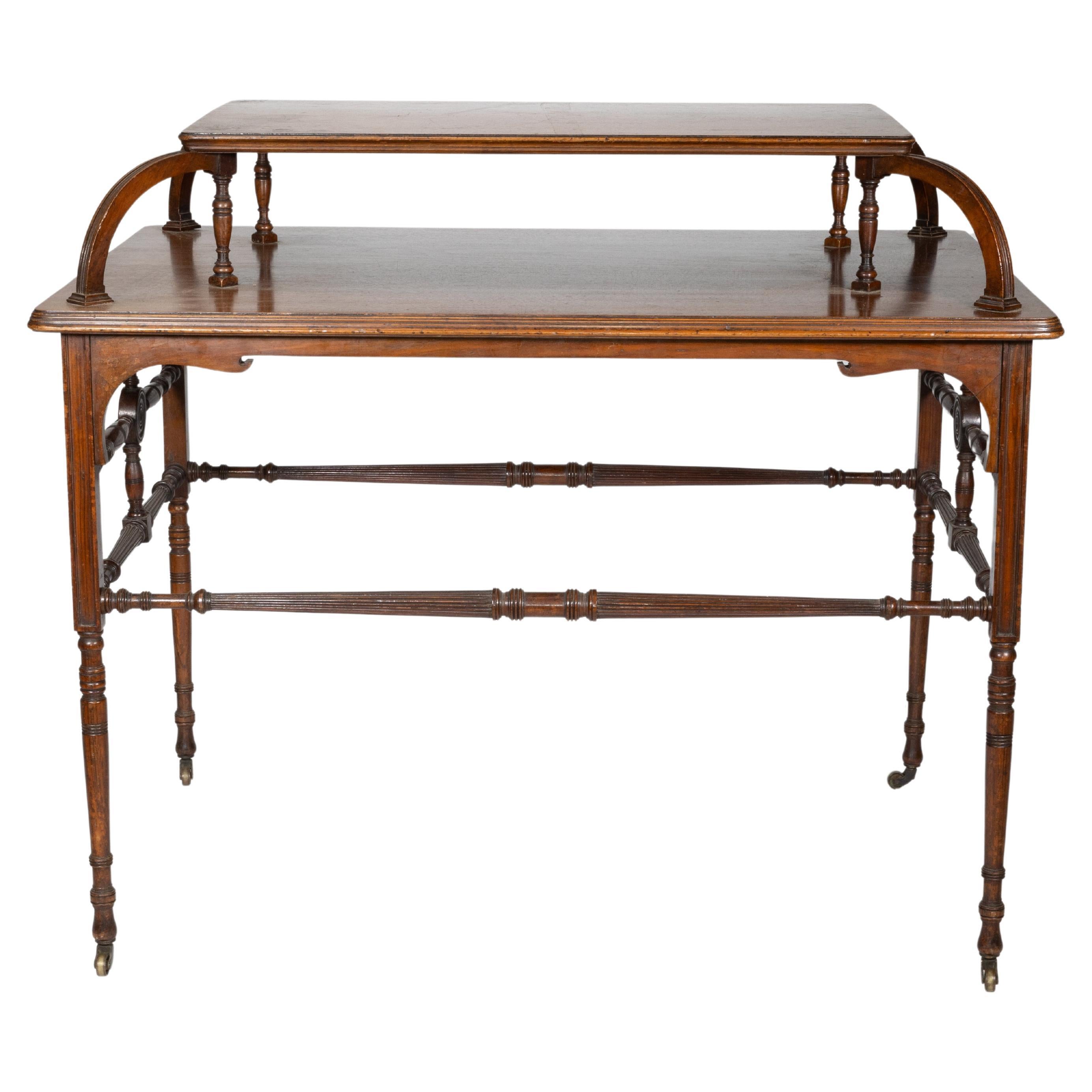 Howard and Sons. A high art Aesthetic Movement walnut centre tea table with an unusual raised upper shelf to the centre of the main top on arched and turned supports. The top with shaped and incised aprons to the corners with fine turned legs united