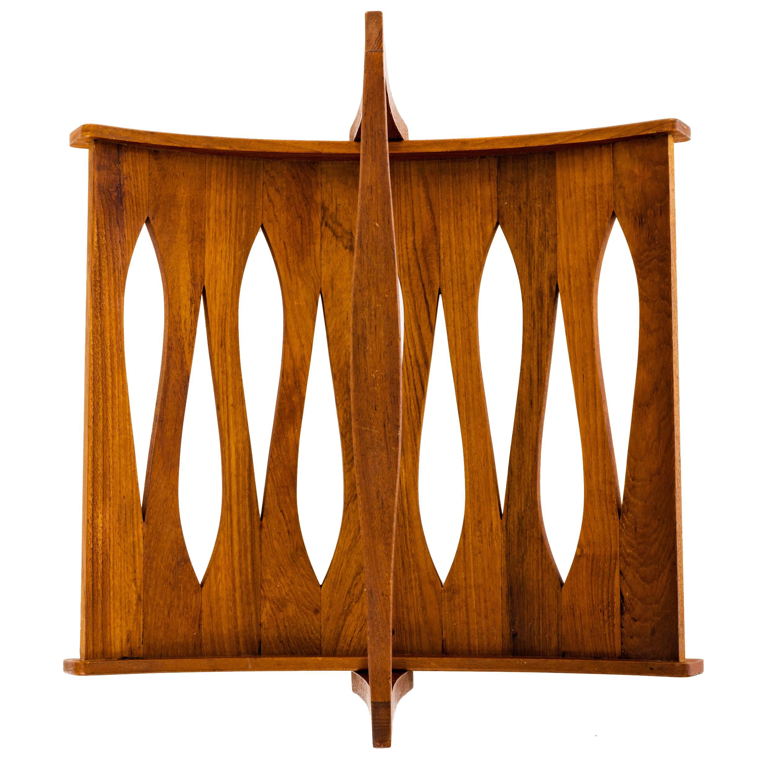 A Danish modern magazine cradle in staved teak designed by Jens Quistgaard for Dansk with a cutout, teardrop-shaped design pattern to the interior and a collapsible handle. Signed with branded mark to underside.