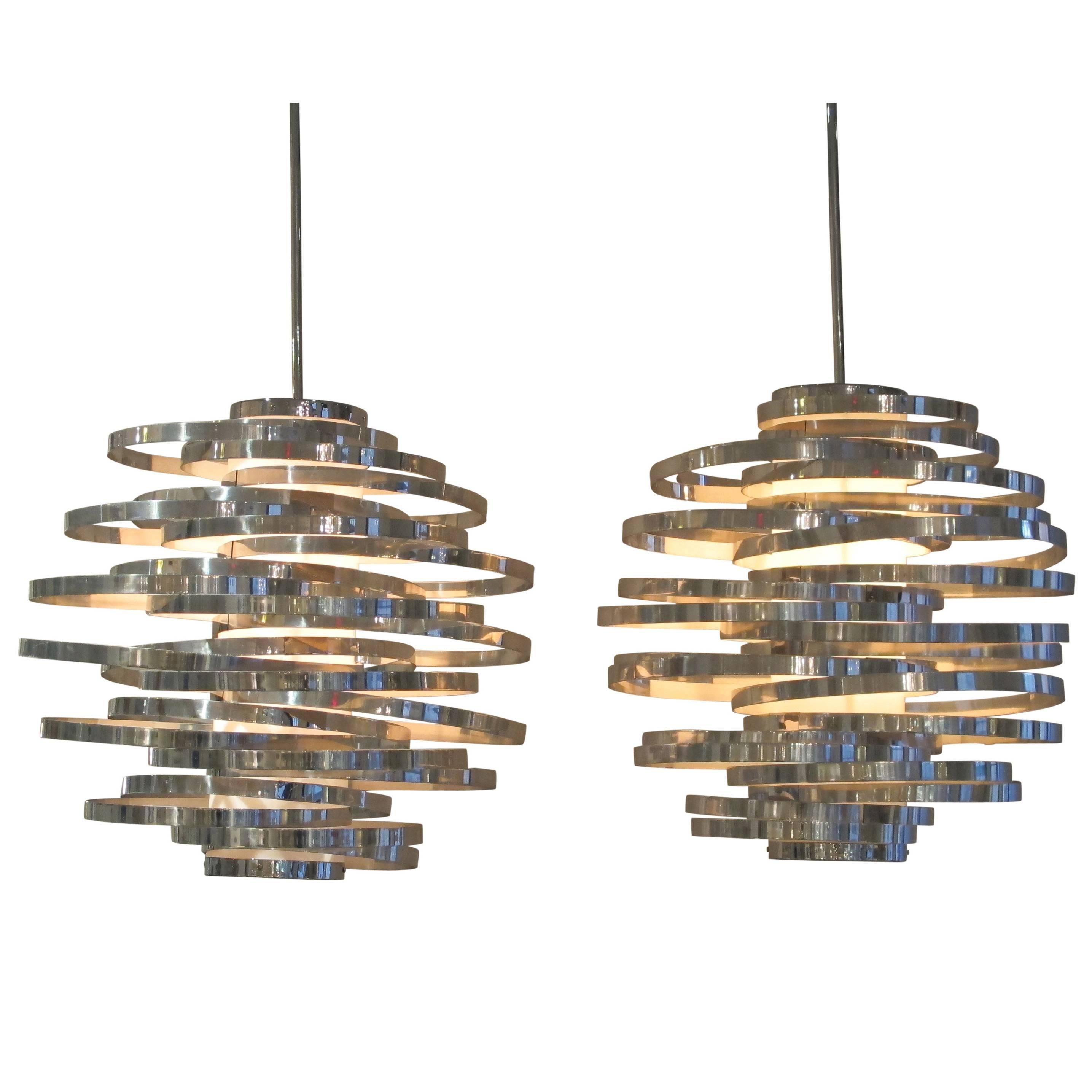 Pair of chromed aluminum cyclone chandeliers, Italy, 1970s. Constructed of polished aluminum bands and a plastic cylinder diffuser. Both fitted with custom three foot round stock rods and round chromed canopies. Rewired for immediate use.
