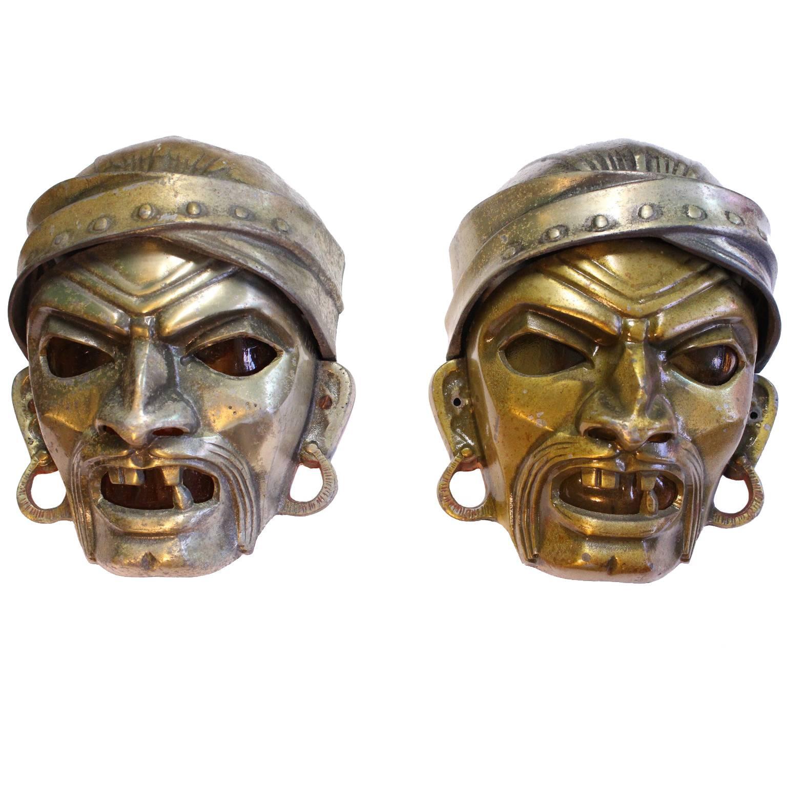 A pair of vintage flush mount wall sconces, produced circa 1930s within the Art Deco period, with cast metal shades formed as grotesque sculptural masks, each face detailed with deep embedded lines, accentuating a furrowed brow and fearsome, mostly