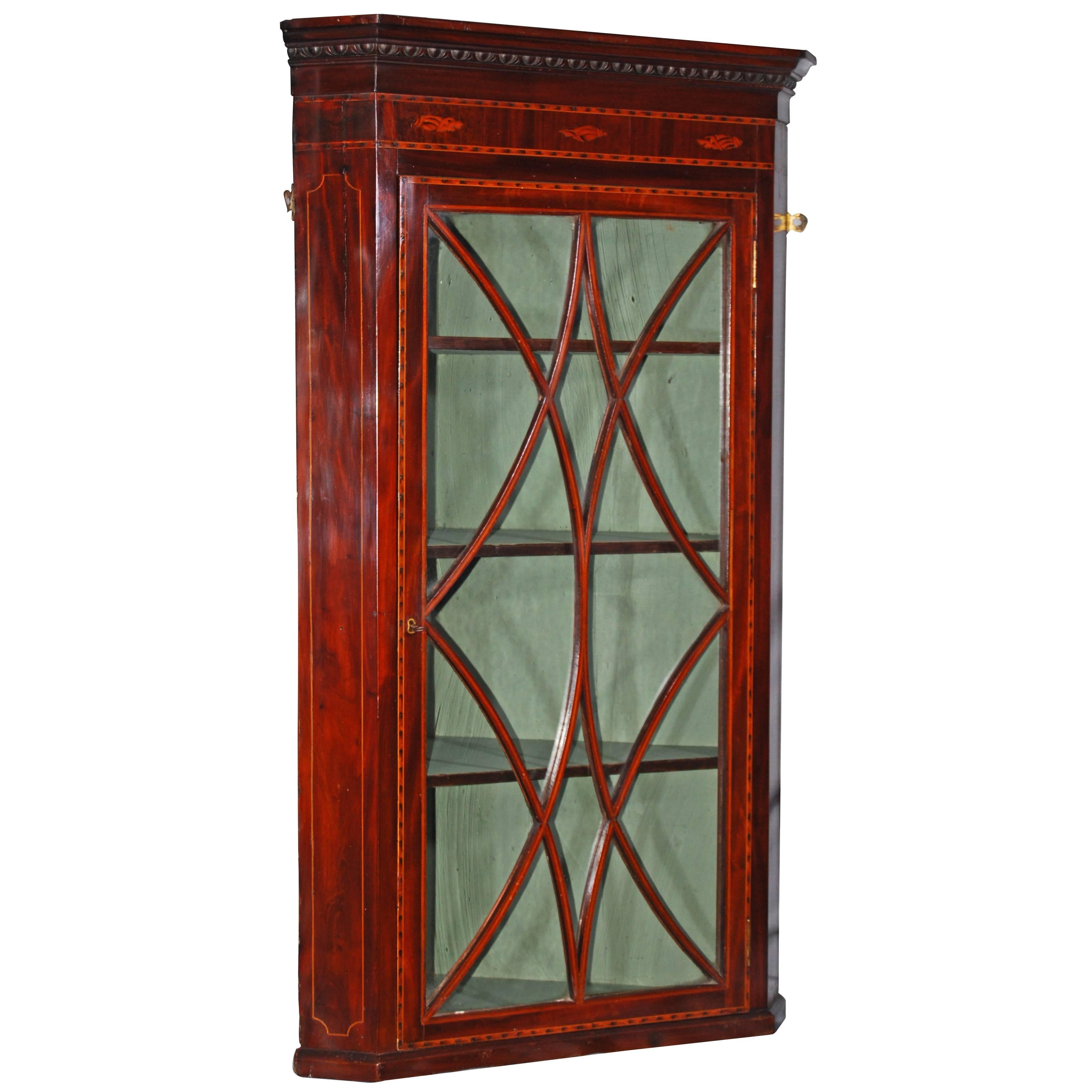 A pretty George III mahogany and inlaid hanging corner cabinet, the stepped cornice above an egg and dart moulding and a frieze inlaid with three shell motifs, the 12 pane diamond glazed door with four shelves behind and the whole feather banded