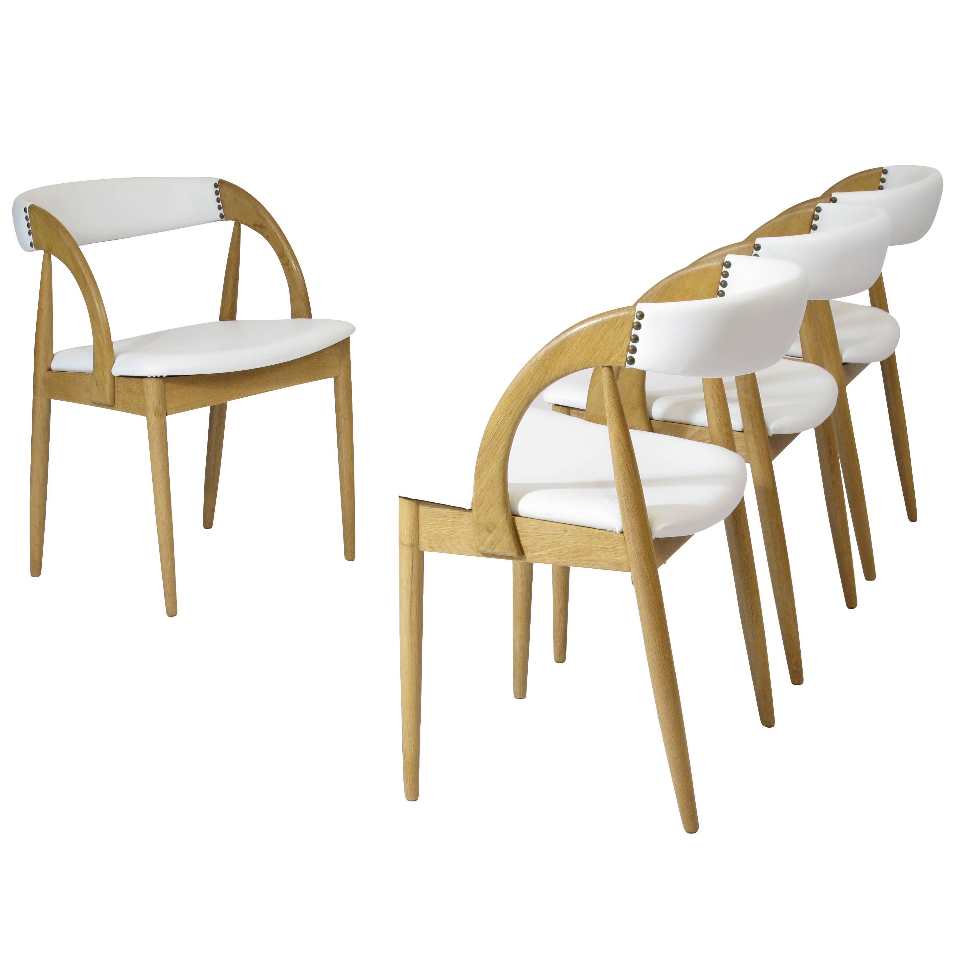 Two mid-century oak dining chairs crafted of solid oak frames newly upholstered with a soft white leather and brass tacks.