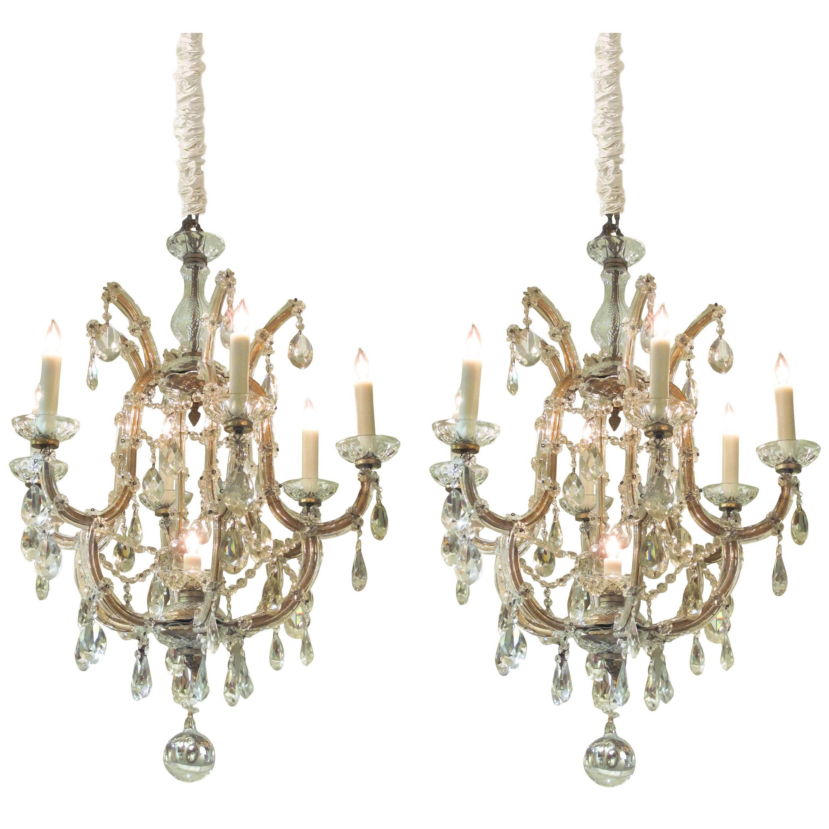 A good pair of continental Maria Theresa basket-form glass and crystal six-light chandeliers; possibly Viennese; composed of hand-forged gilt-metal frames sheathed in glass; emanating 6 scrolled candle-arms with a central light within the fixture.