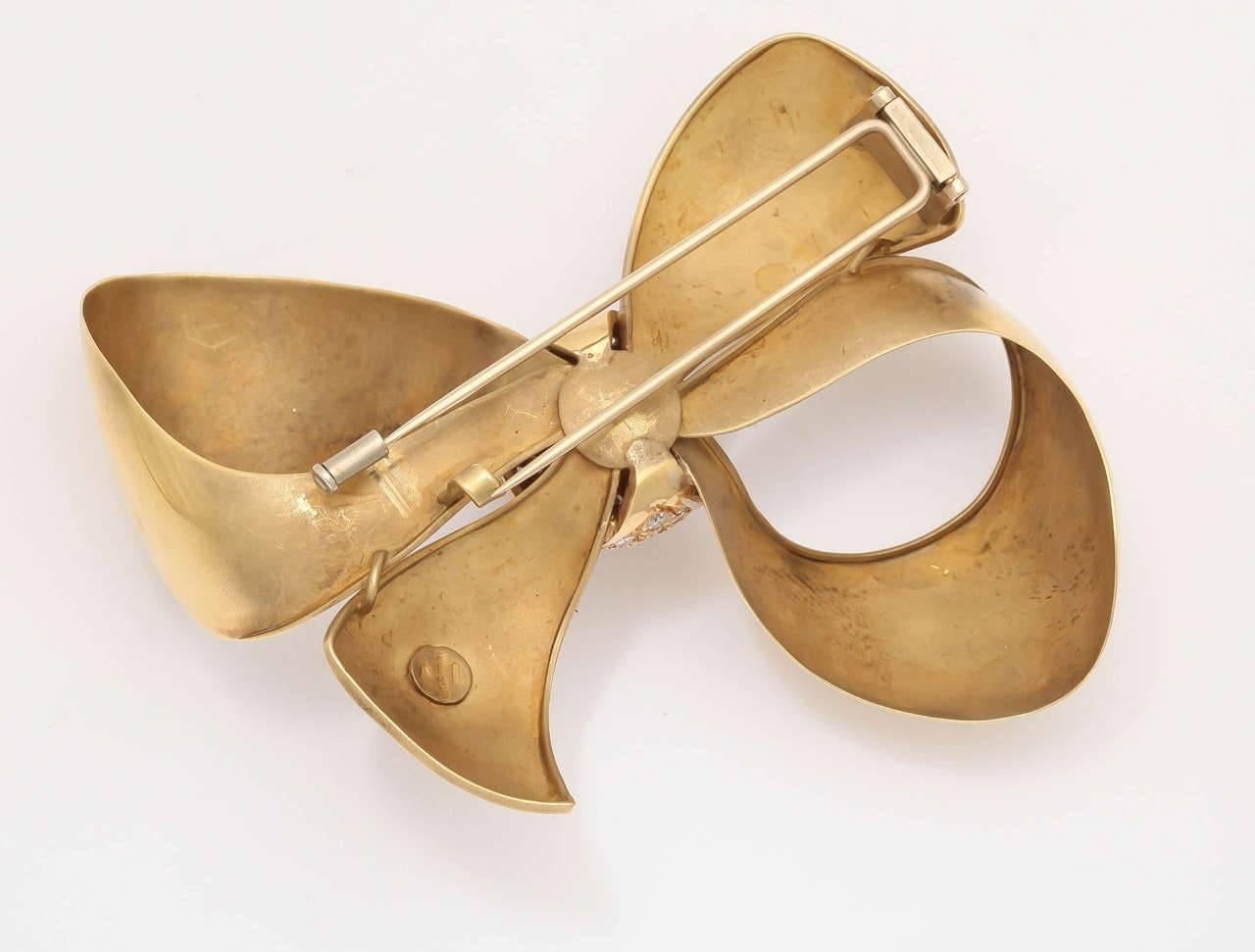 A statement bow in 18 kt gold with varying finishes by an Italian designer with a cluster of individually set diamonds with makers mark and can be worn either as a pin or as a pendant on a necklace.
