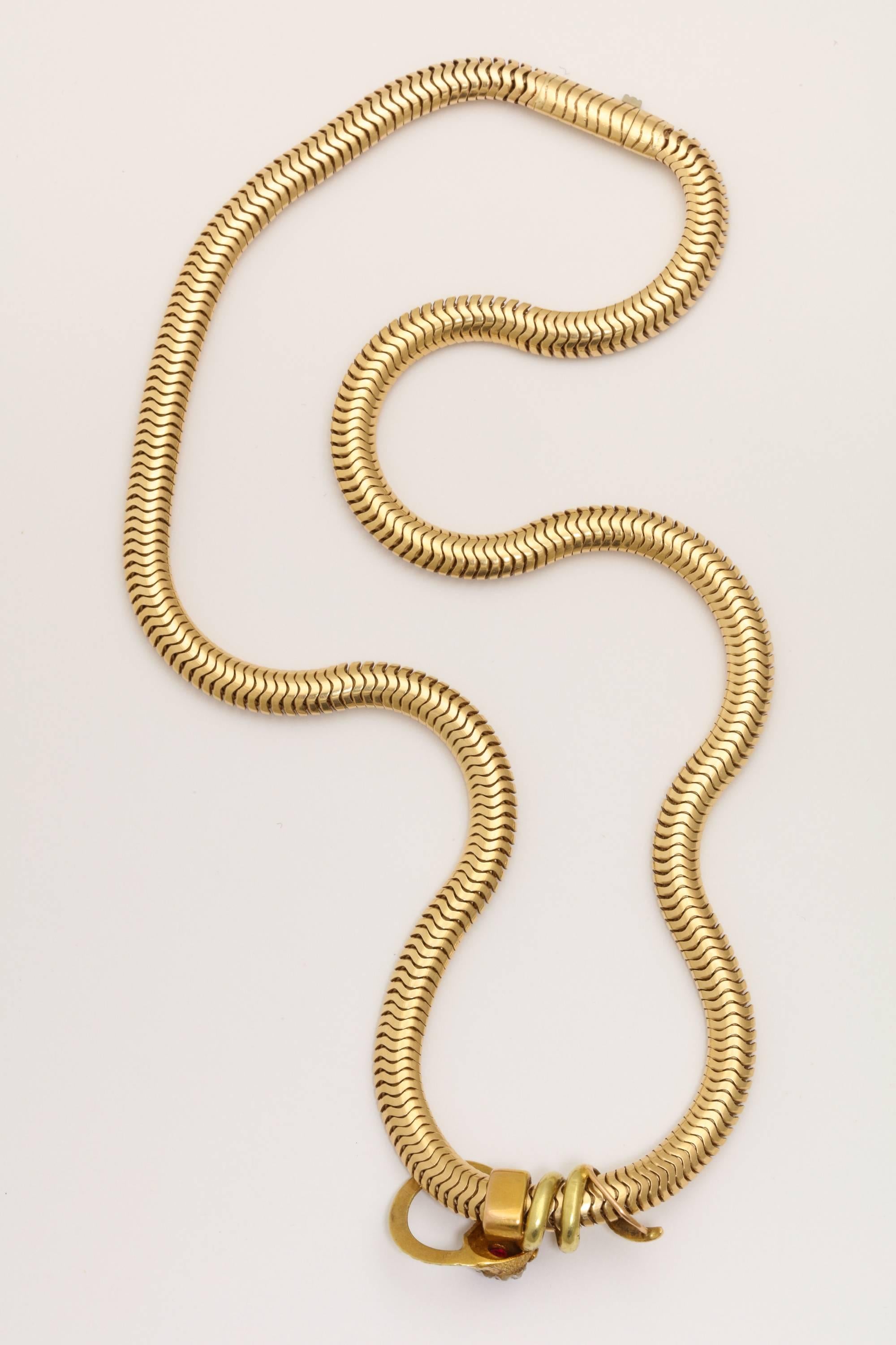 A great example of a classic 1930s 18-karat gold snake coiled around a woven 14-karat gold snake chain. The headb is encrusted with a ruby crest and surrounded by mine diamonds with ruby eyes and pearl.