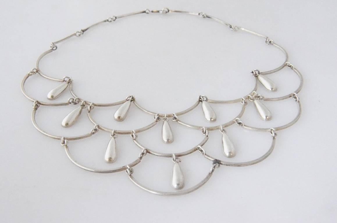 Being offered is a circa 1960 .970 silver necklace by Antonio Pineda, of Taxco, Mexico in a bib motif, with cascading 1 inch long silver 'droplets' in the multiple tiers.  Necklace is 16 ½ inches long, not a choker, and the drop in the first tier is