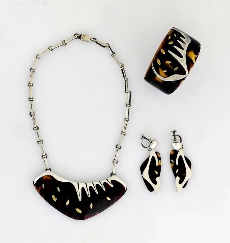 Being offered is  a circa 1953 exceedingly rare jewelry set by Enrique Ledesma of Taxco, Mexico. Consisting of a necklace, cuff bracelet & earrings made primarily of shell, with applied silver and brass biomorphic motifs. Dimensions:  necklace