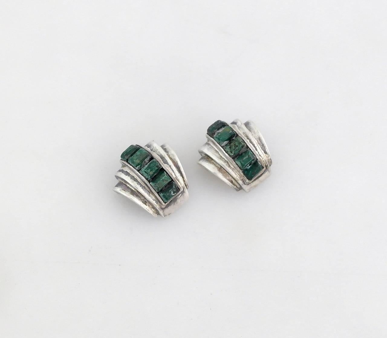 Being offered are a pair of circa 1955 .970 silver pins by Antonio Pineda of Taxco, Mexico. Pins adorned with Mexican jade stone, set in a sleek modernist design. Dimensions: 1 inch by 1 inch.  Marked as illustrated. In excellent condition. 