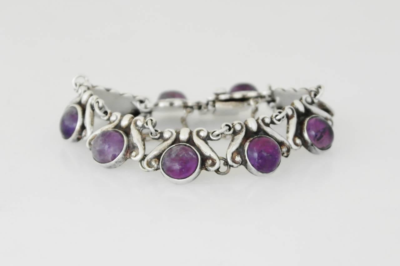 Being offered is a circa 1968 sterling silver bracelet by Los Castillo of Taxco, Mexico. Each link decorated with a scroll & bead design and bezel set amethyst cabochons. Dimensions: 3/4" wide; inner dimensions 7 1/2". Weight 1.5 oz.