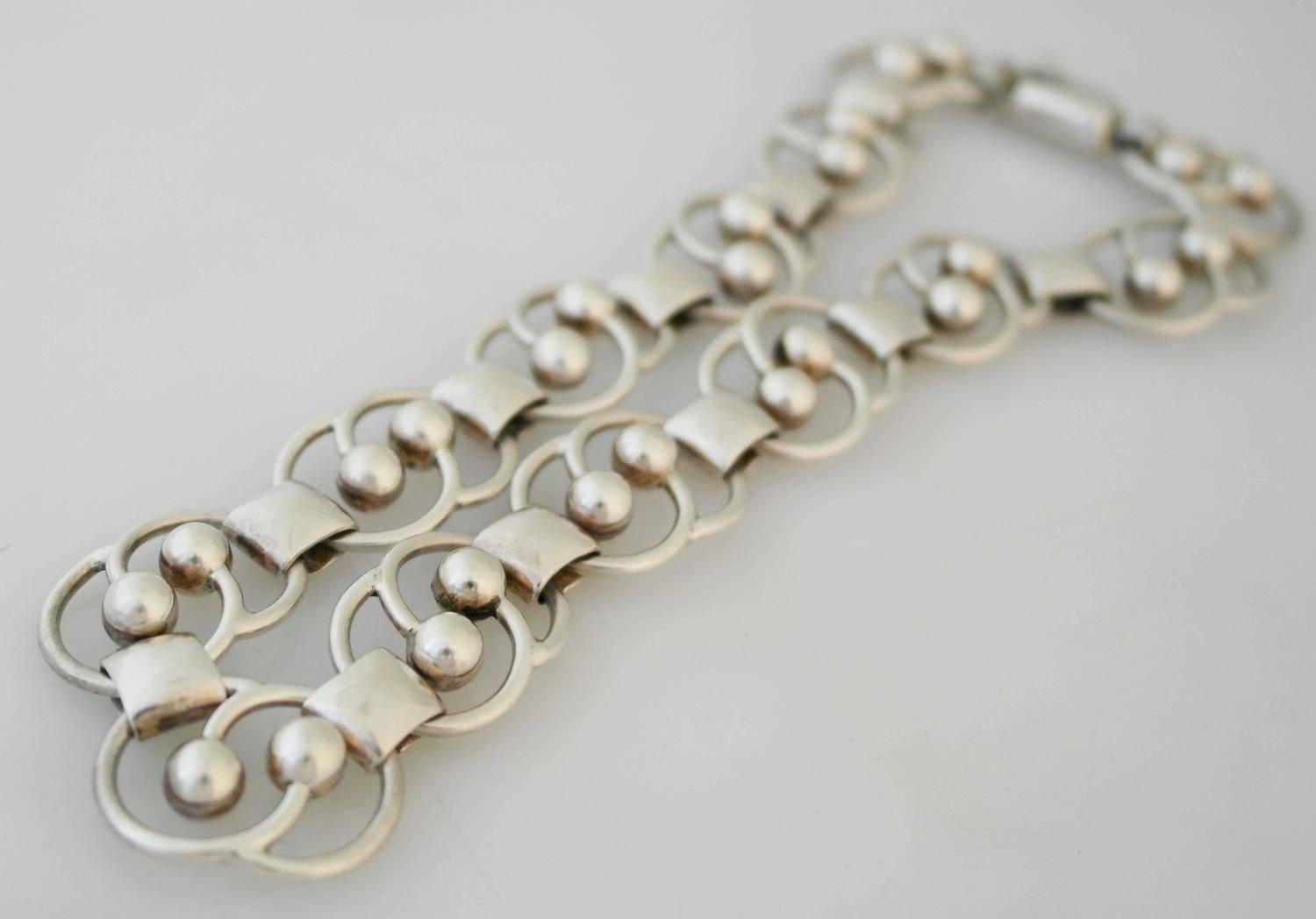 Being offered is a circa 1955 sterling silver necklace by Hector Aguilar of Taxco, Mexico. Comprising intertwining circular links with beaded silver motifs; tongue & box closure. Dimensions: 1/2" wide x 15" wearable length. Marked as
