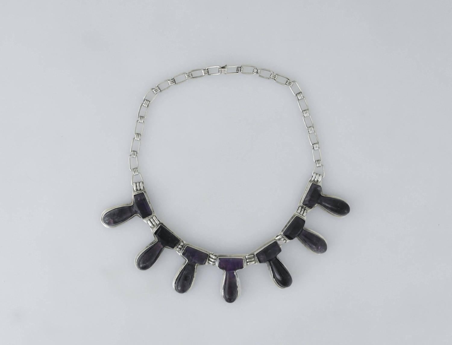 Being offered is a sterling silver necklace made in Taxco, Mexico (maker unknown). Early necklace decorated with seven amethyst decorated drop links; hook closure. Dimensions: 16 inches x 1 1/2 inches wide. Marked as illustrated. In excellent
