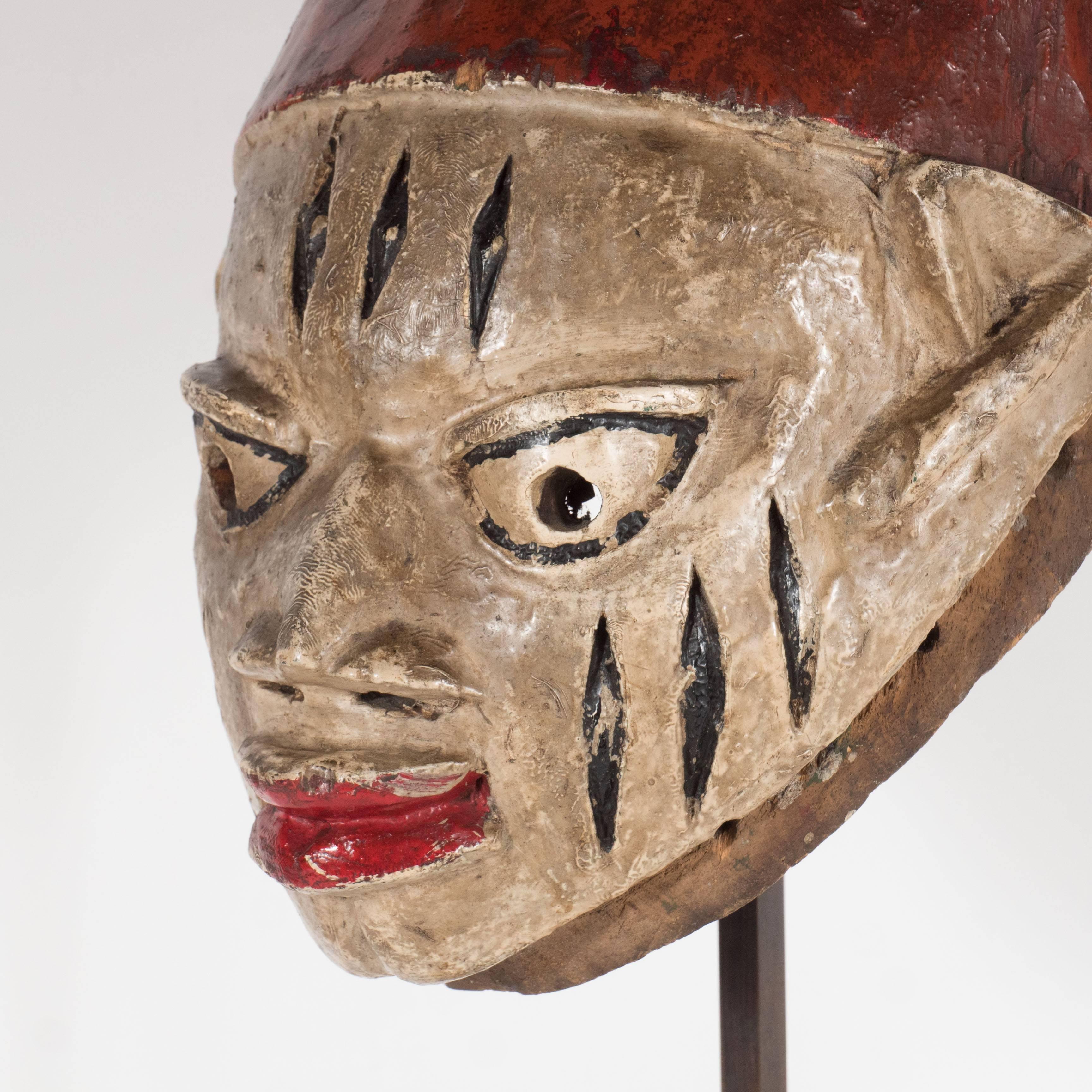 A painted head crest mask which appears to be from a 'Gelede cult,' known for honoring women and fertility, in the state of Benin (formerly Dahomey) in Nigeria, 20th century. This bust features three sets of vertical striations on the figure's