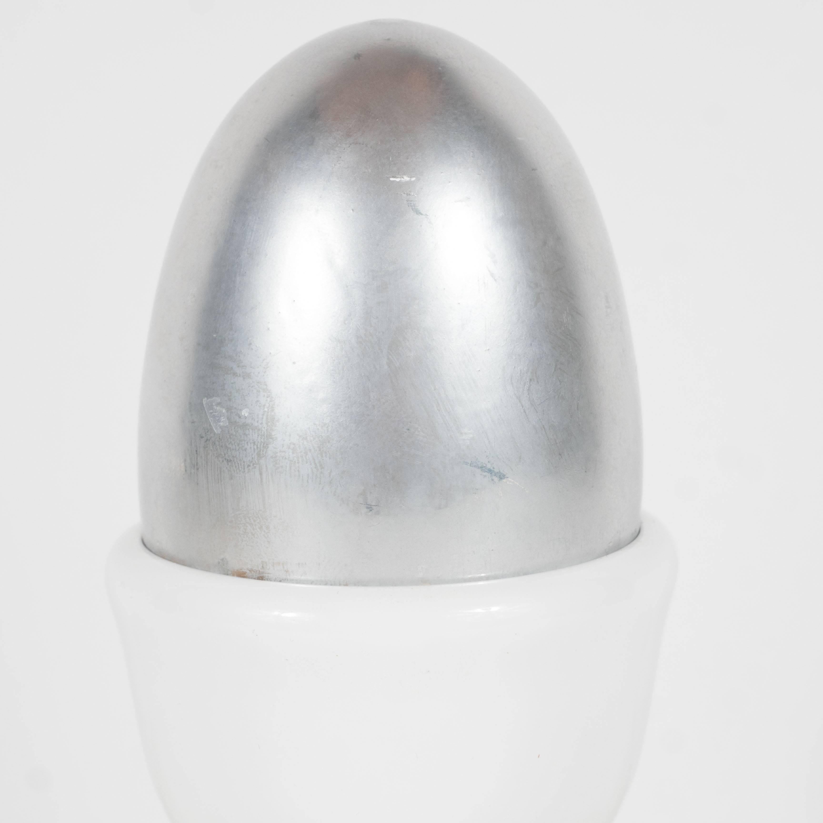 This sculpture, in the form of a silver electroplated egg with a white porcelain holder, represents esteemed Swiss artist Herbert Distel's most iconic form. He created a 22-ton egg during this same period, which he installed on the road between