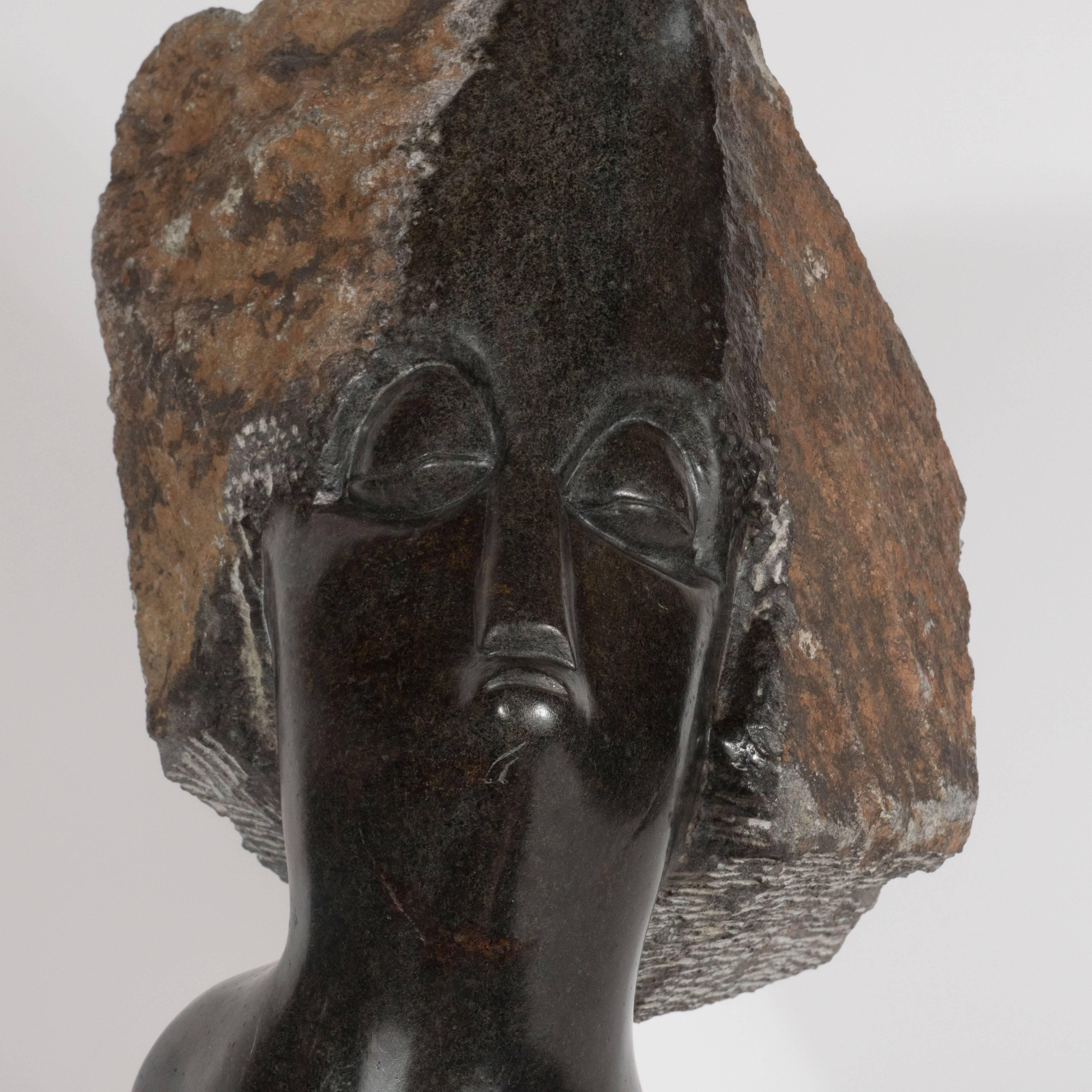 This impressive sculpture represents the marriage of tribal art with western techniques and materials. Realized in the style of Constantin Brancusi, this figurative bust presents a stylized face chiseled into black marble. The female visage appears