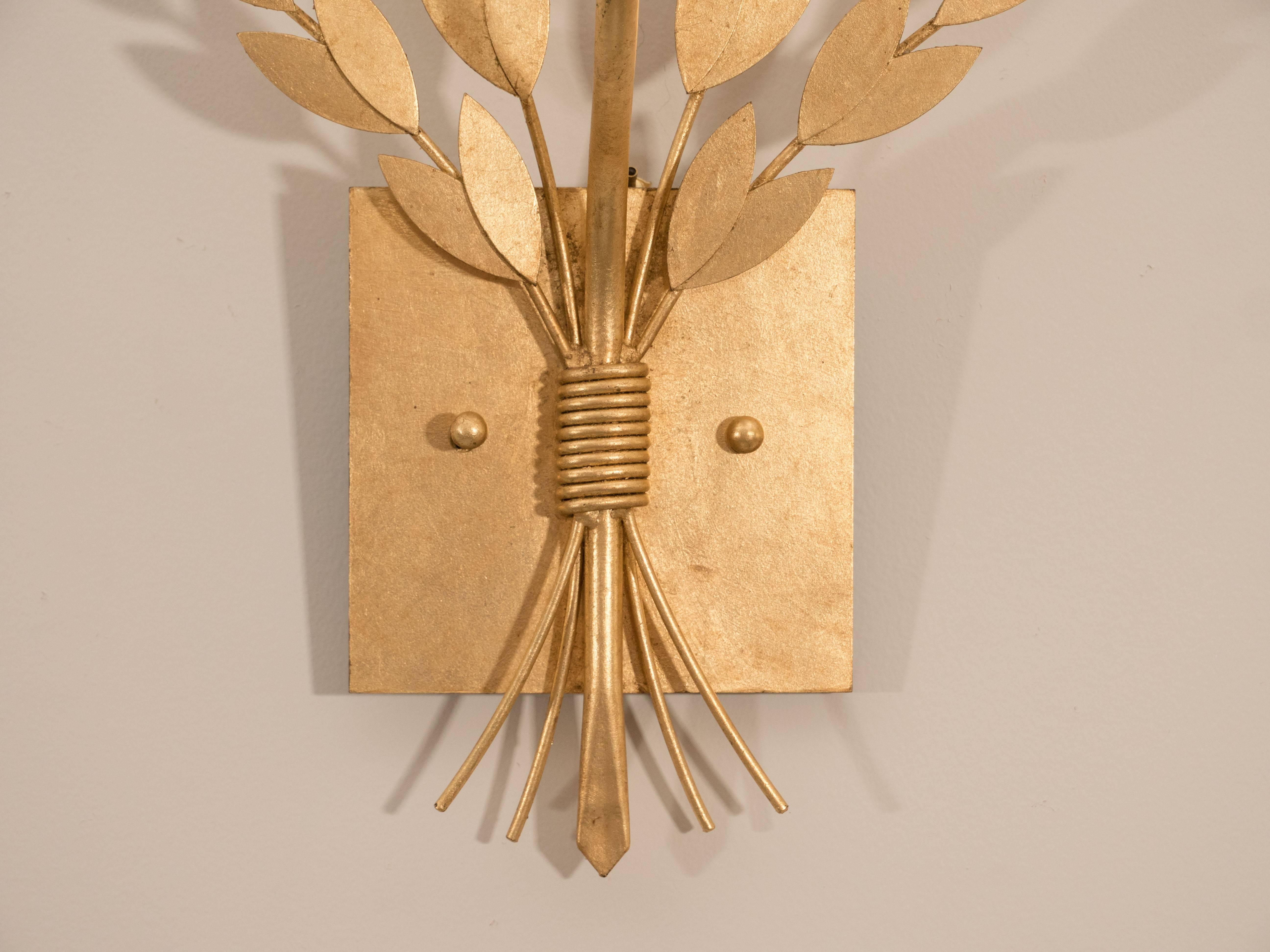 We love these sconces for their simple elegance. They have just enough detail to make them interesting, but not fussy. These one-arm wall lights are composed of gilt metal, with a square back plate and small branches of decorative leaves. Designed