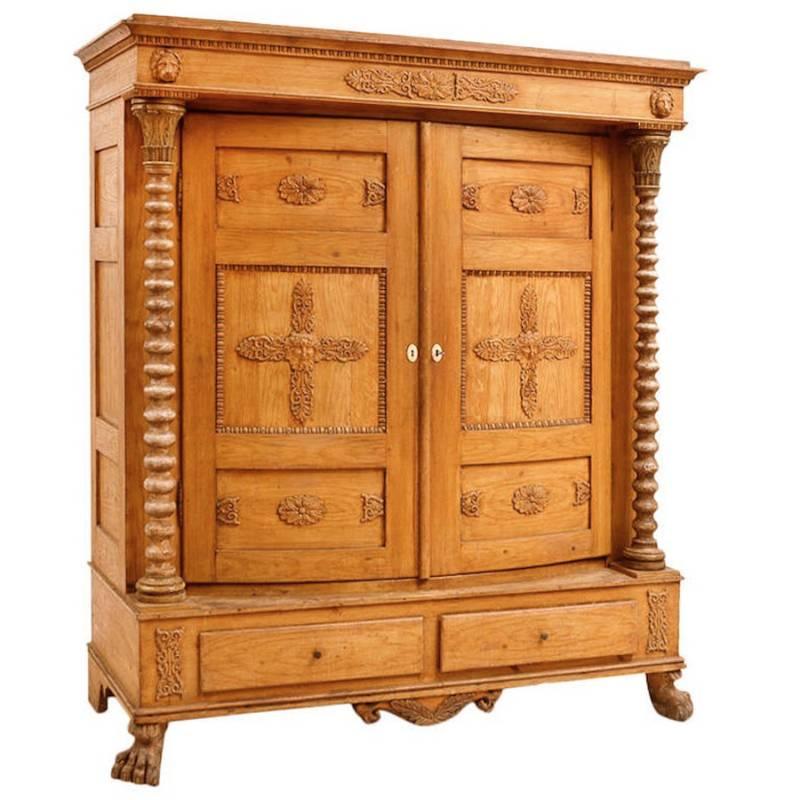 A very charming and unique armoire in the original ochre-colored, faux bois finish, with bowed front doors decorated with carved rosettes, palmettes and Bacchus heads that are flanked by spool-turned columns with carved and painted green acanthus