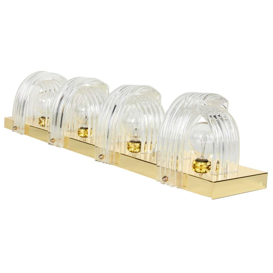 Hollywood Regency mid-century wall light comprised of polished brass frame, with sculptural shades comprised of molded lucite. The four series of curved Lucite rings create beautiful prism lighting, while concealing the light bulbs. Perfect lighting